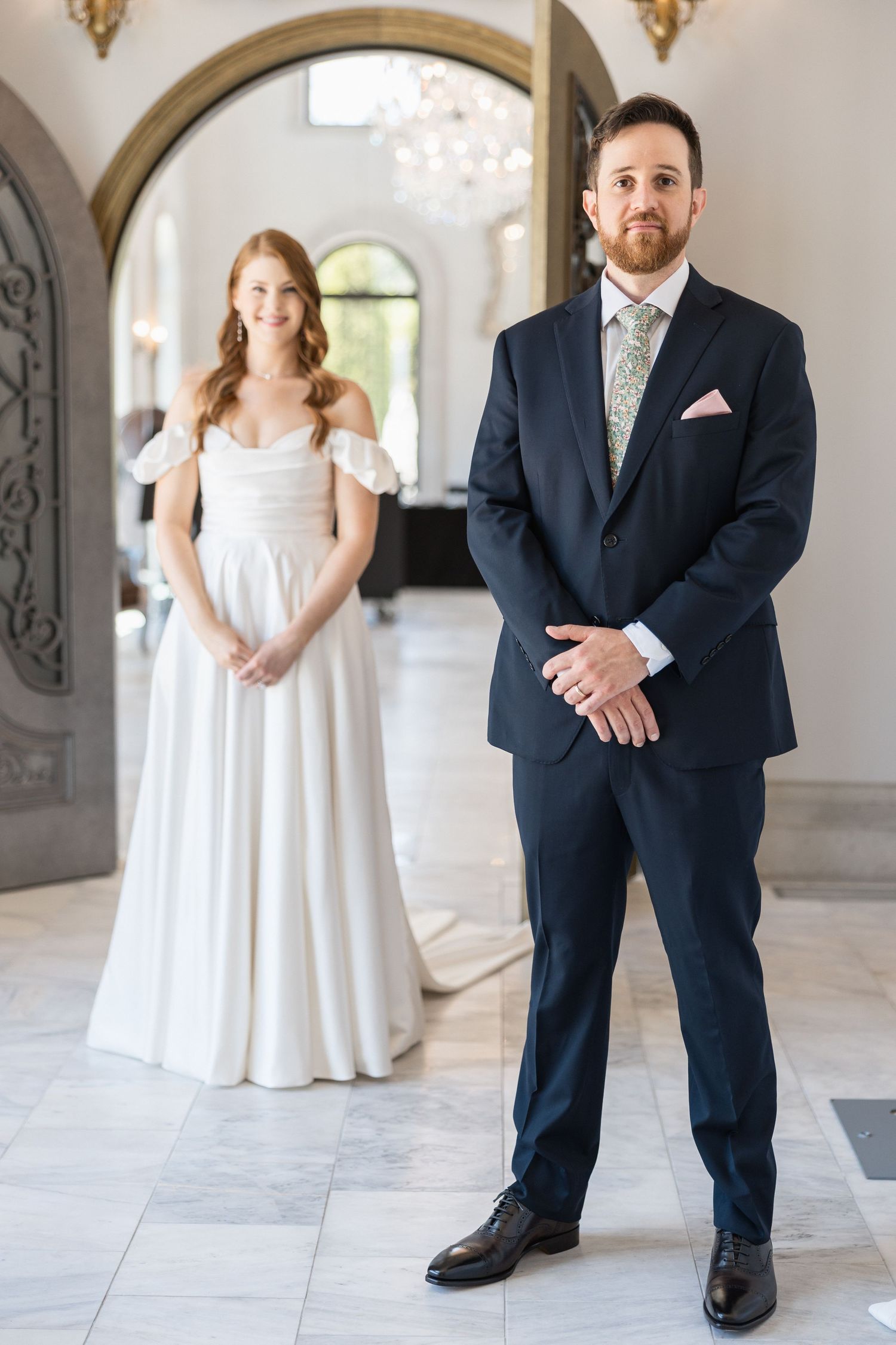 Wedding couple shares candid moments in bright indoor venue with arched doorways.