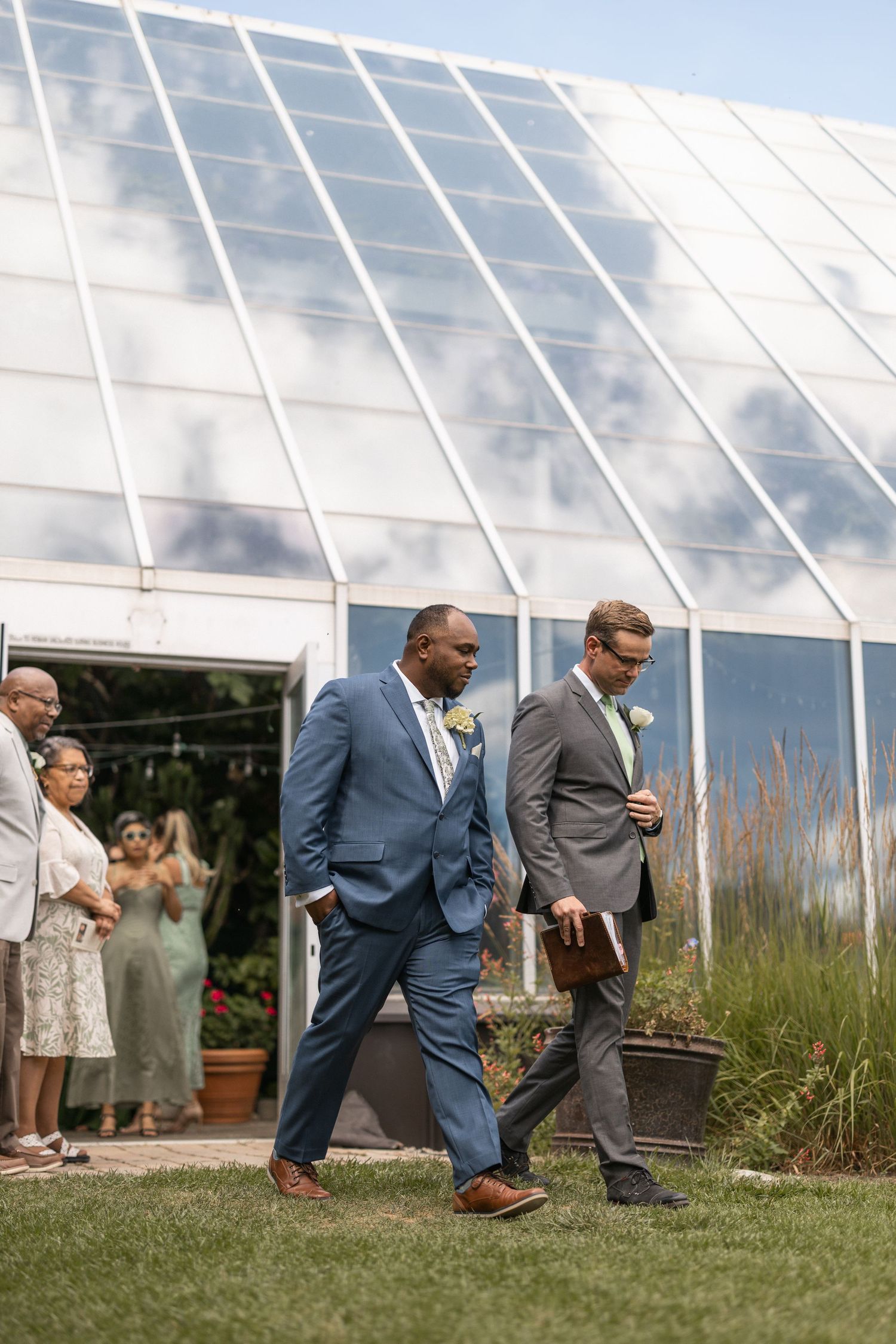 Wedding guests gathering outside a large greenhouse venue.