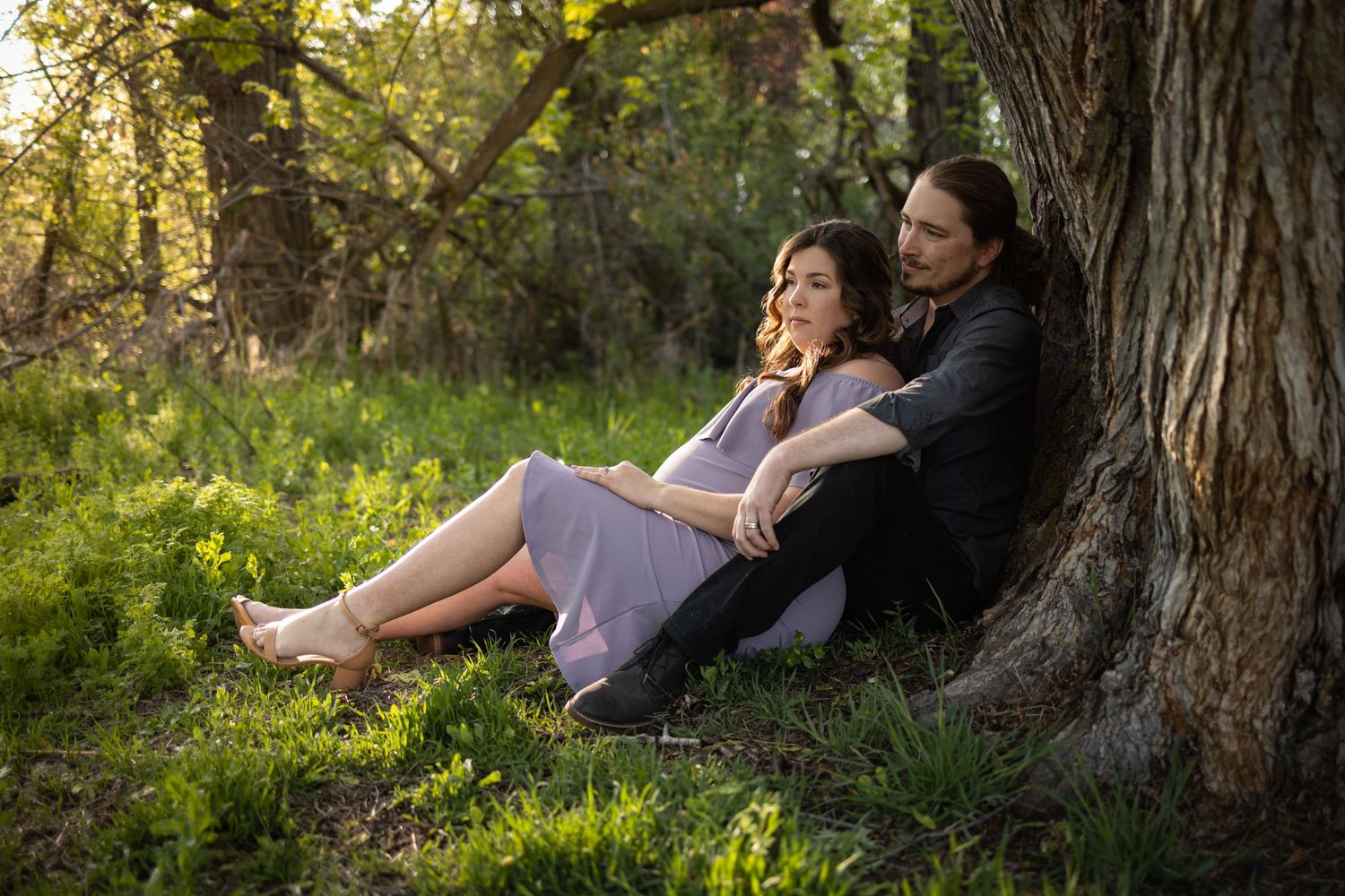 Couple relaxing under a large tree in a sunlit meadow during golden hour.