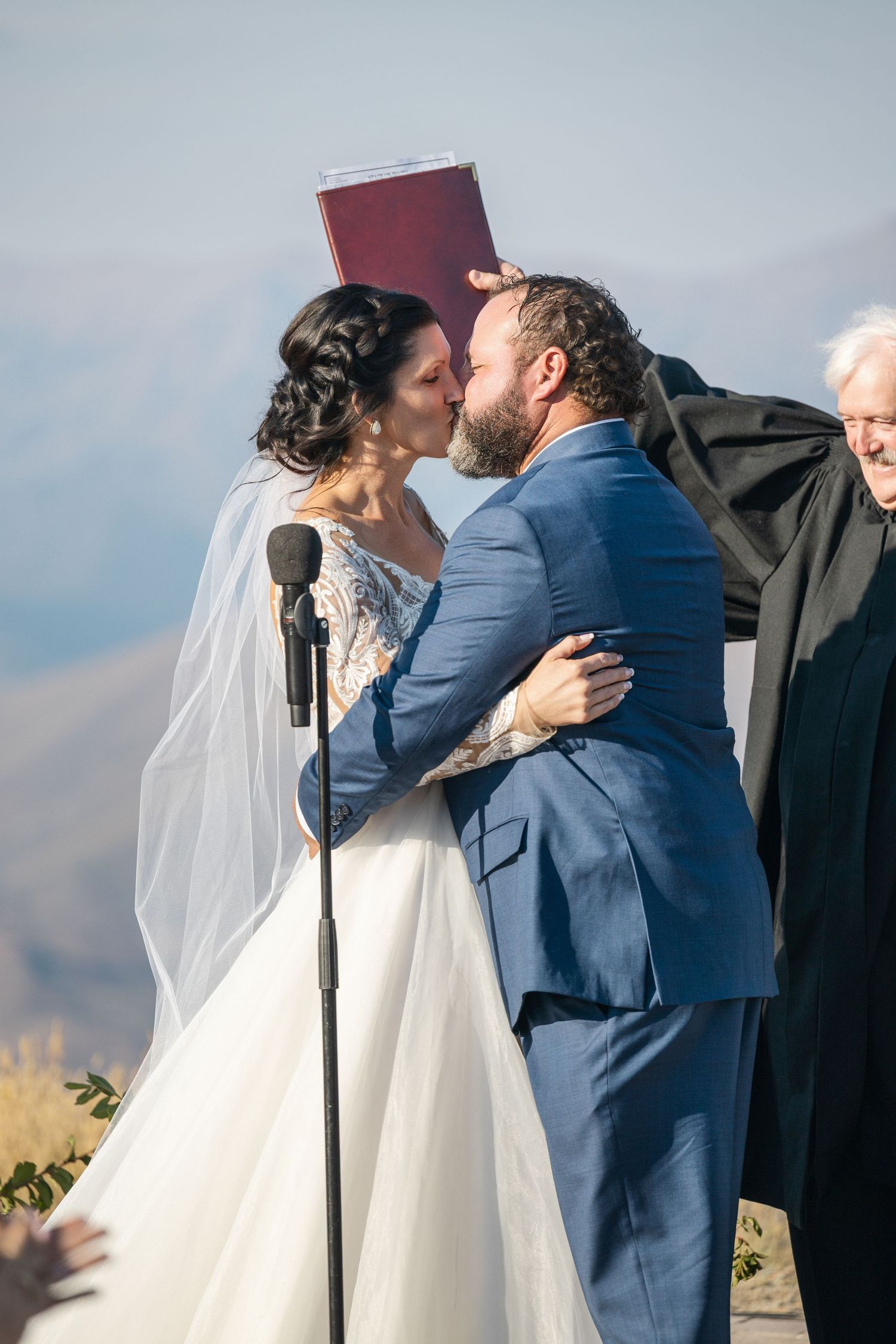 A couple shares their first kiss as newlyweds during a mountain wedding ceremony.