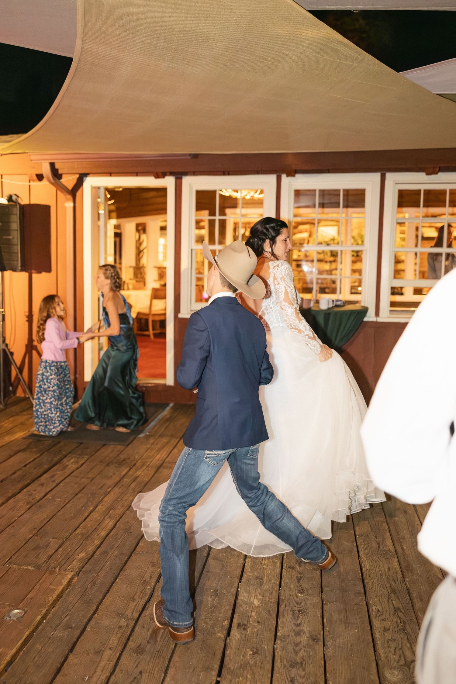Wedding reception on wooden deck with guests dancing around flowing white wedding dresses.