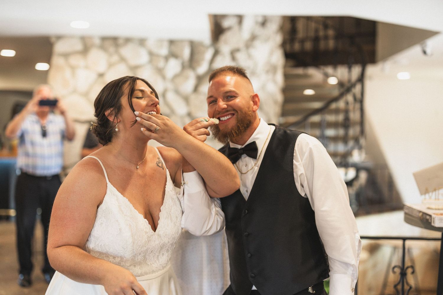 Wedding couple sharing cake during reception celebration at stone venue.
