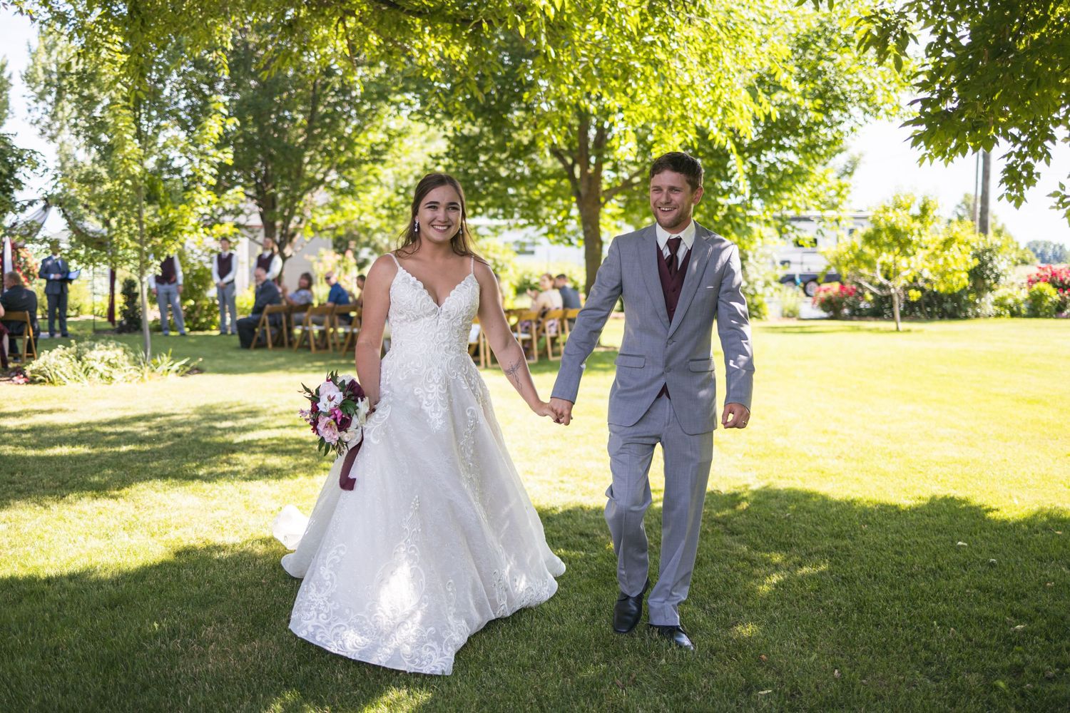 Newlyweds walking hand in hand on grass after outdoor wedding ceremony.