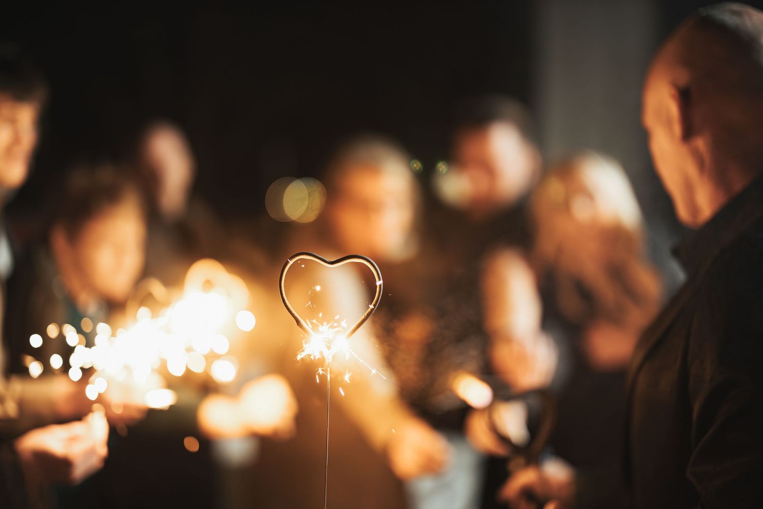 Glowing heart-shaped sparkler against dark background at wedding reception.