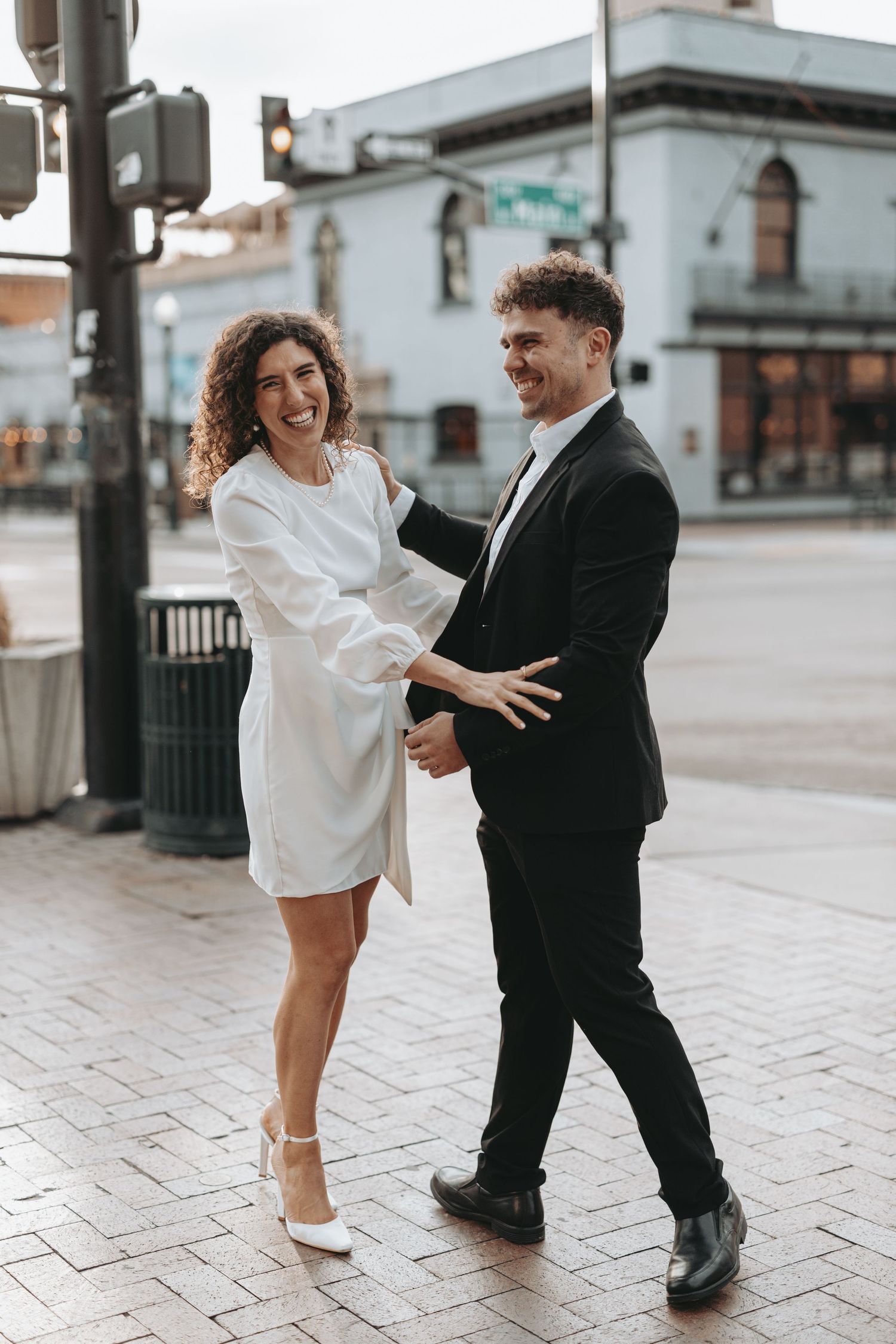 A joyful couple dancing and laughing together on a downtown sidewalk.