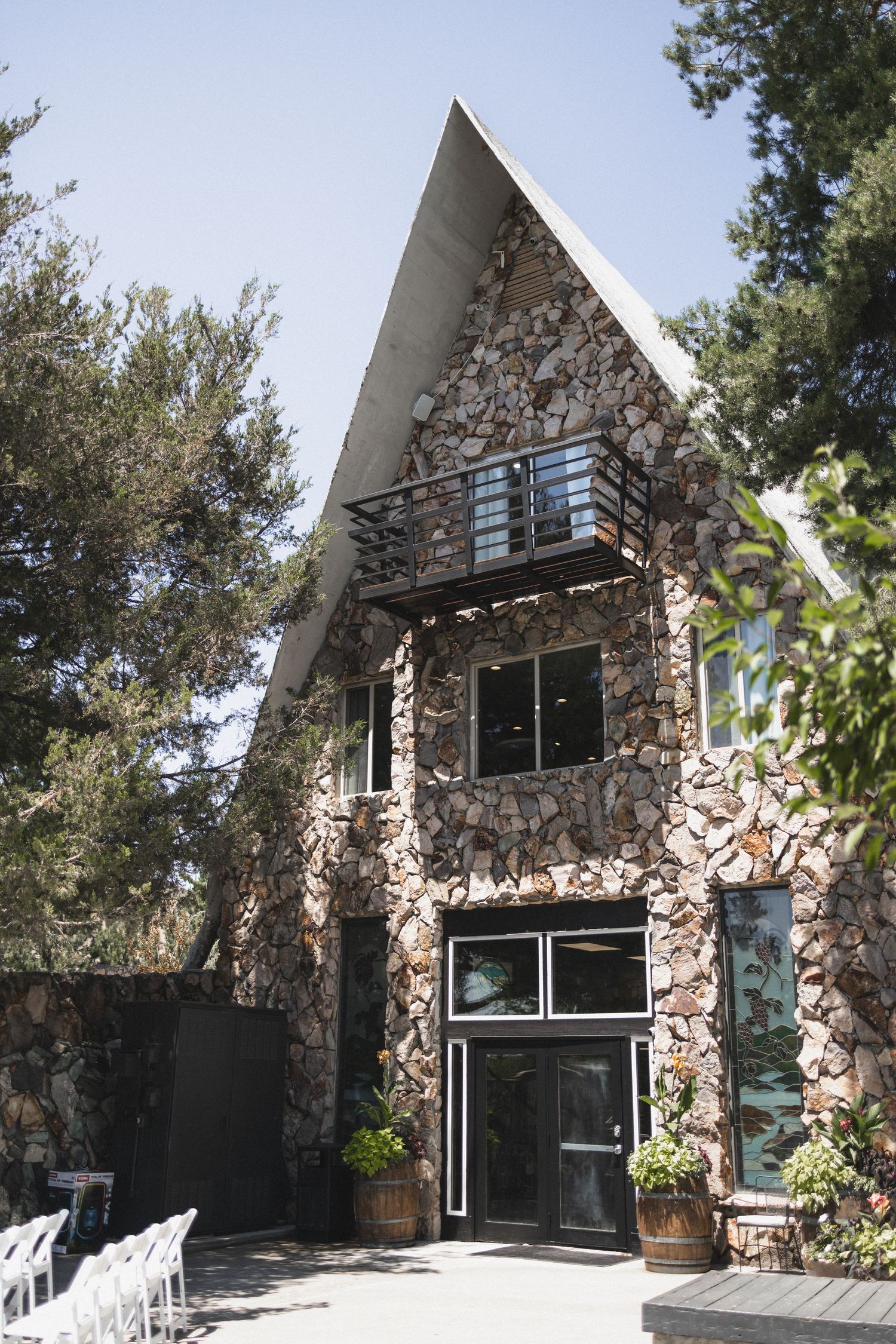 A-frame stone chapel with modern windows and wooden entrance doors surrounded by pine trees.