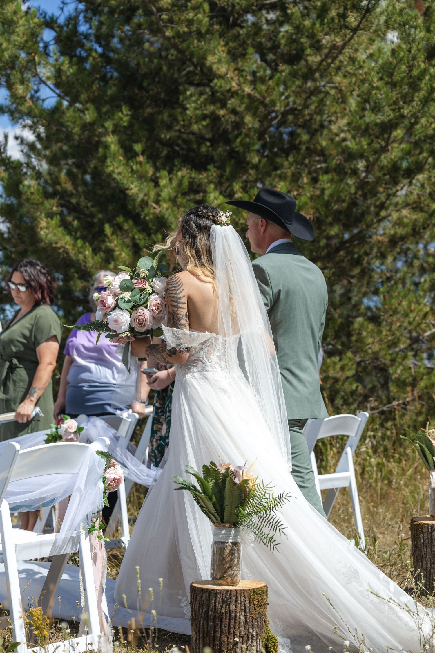 Outdoor wedding ceremony with white chairs and rustic tree stump decorations in a natural setting.