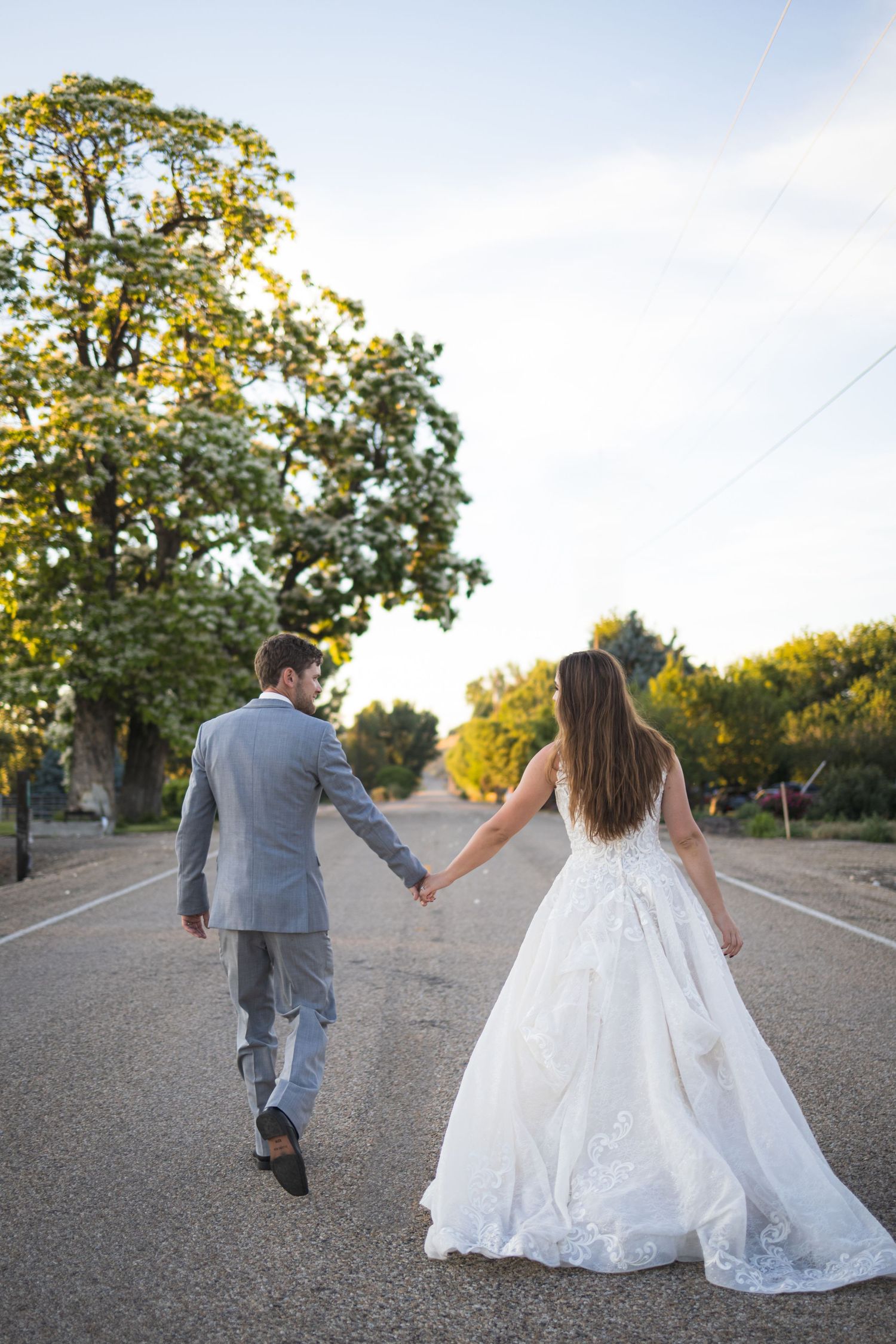 A bride and groom walking hand in hand down an empty road during their wedding photoshoot.