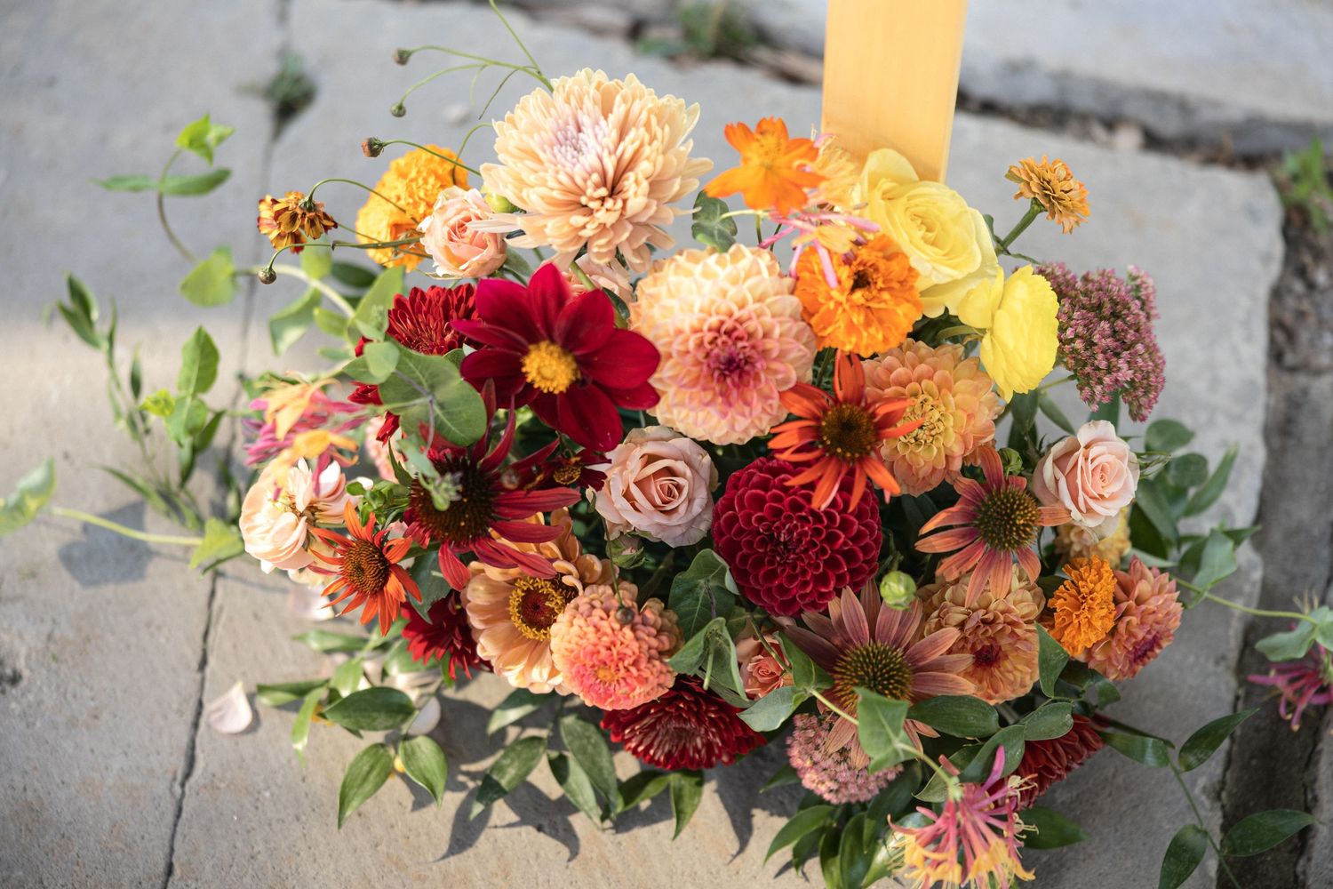 Vibrant fall wedding bouquet featuring dahlias, roses, and ranunculus in coral, burgundy, and peach tones.