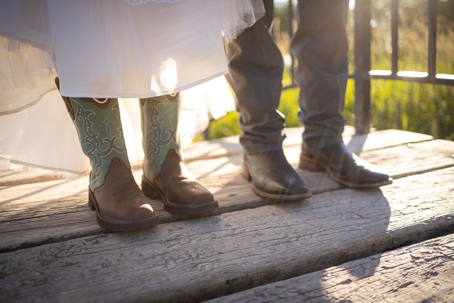 Couple's boots standing together on wooden deck, showing contrast between dress and casual footwear.