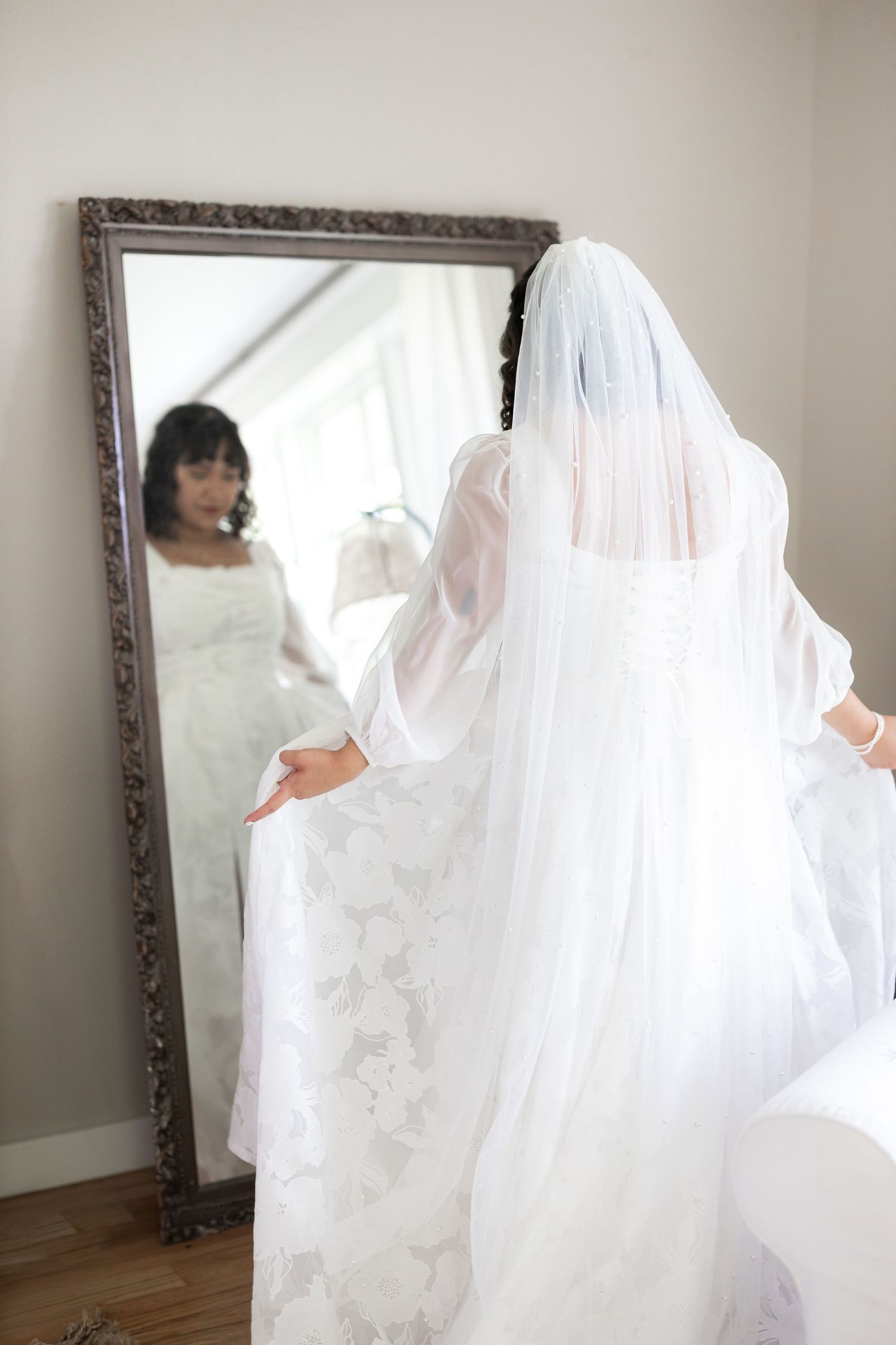 White wedding dress and veil reflection in ornate framed mirror.