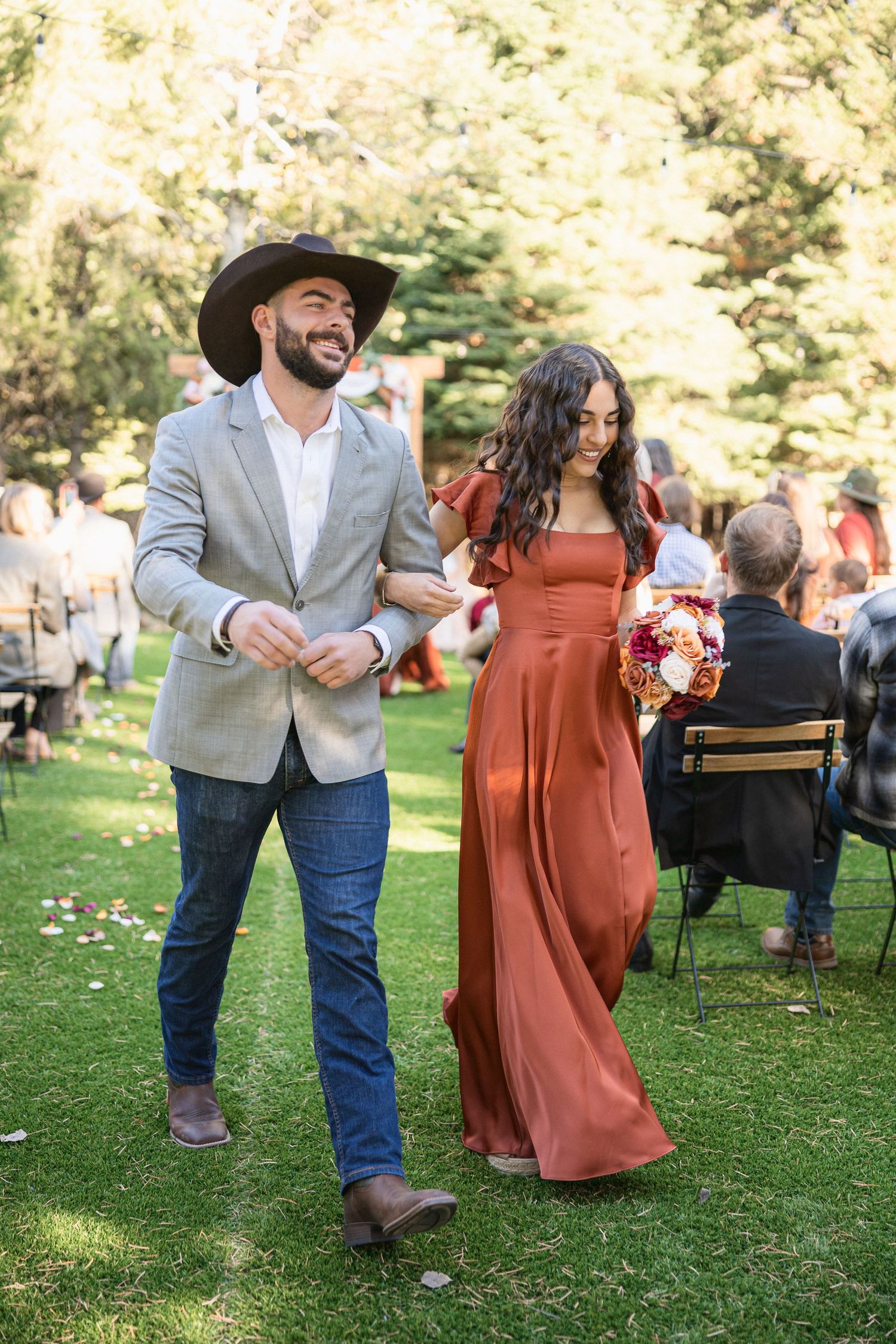 A couple in western attire dances together at an outdoor celebration, with the woman wearing a rust-colored dress.