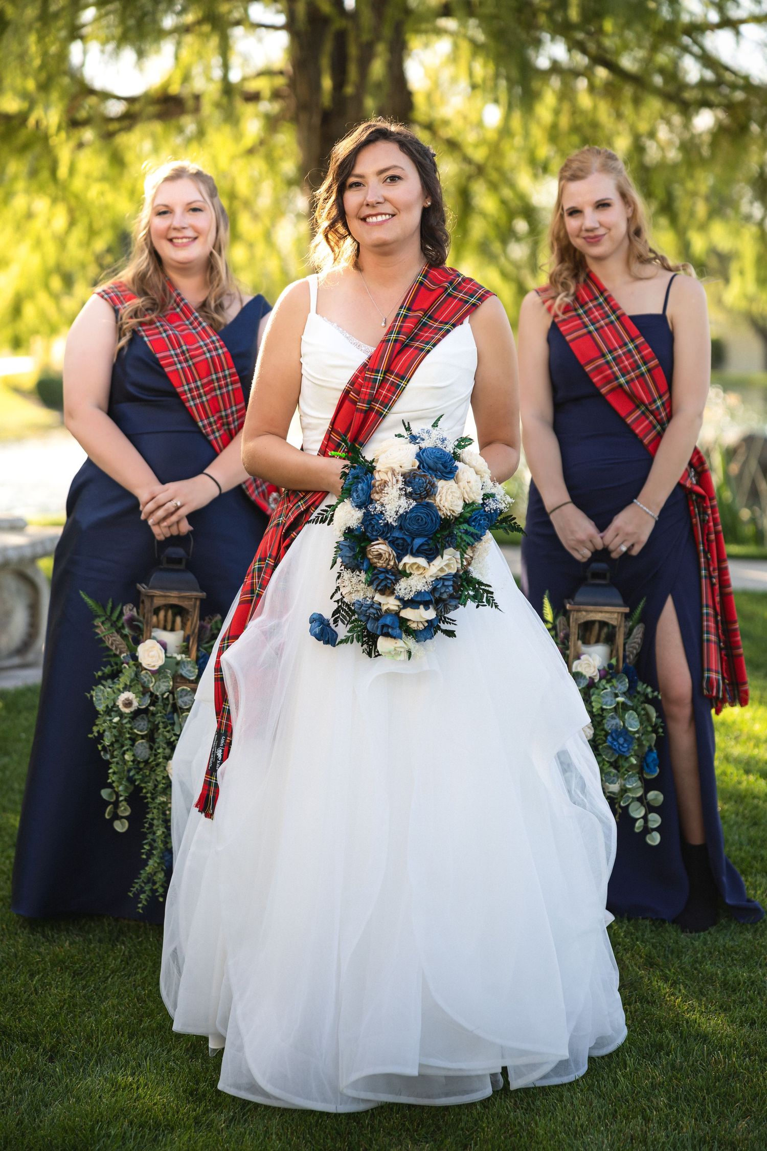 Bride and bridesmaids smile in coordinated navy and tartan Scottish-themed wedding attire.