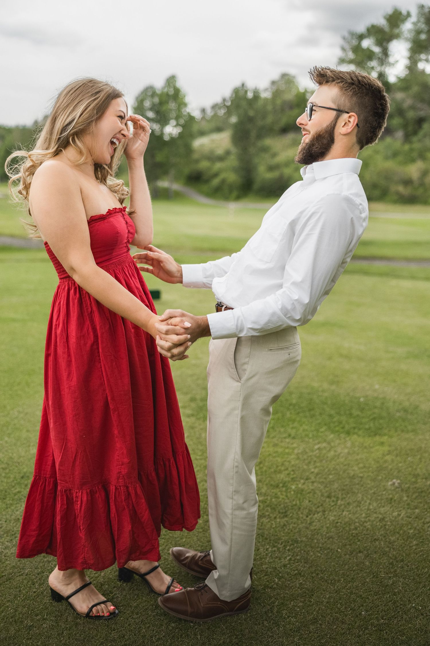 A couple shares a joyful moment on a golf course, with one wearing a red dress and the other in a white shirt.