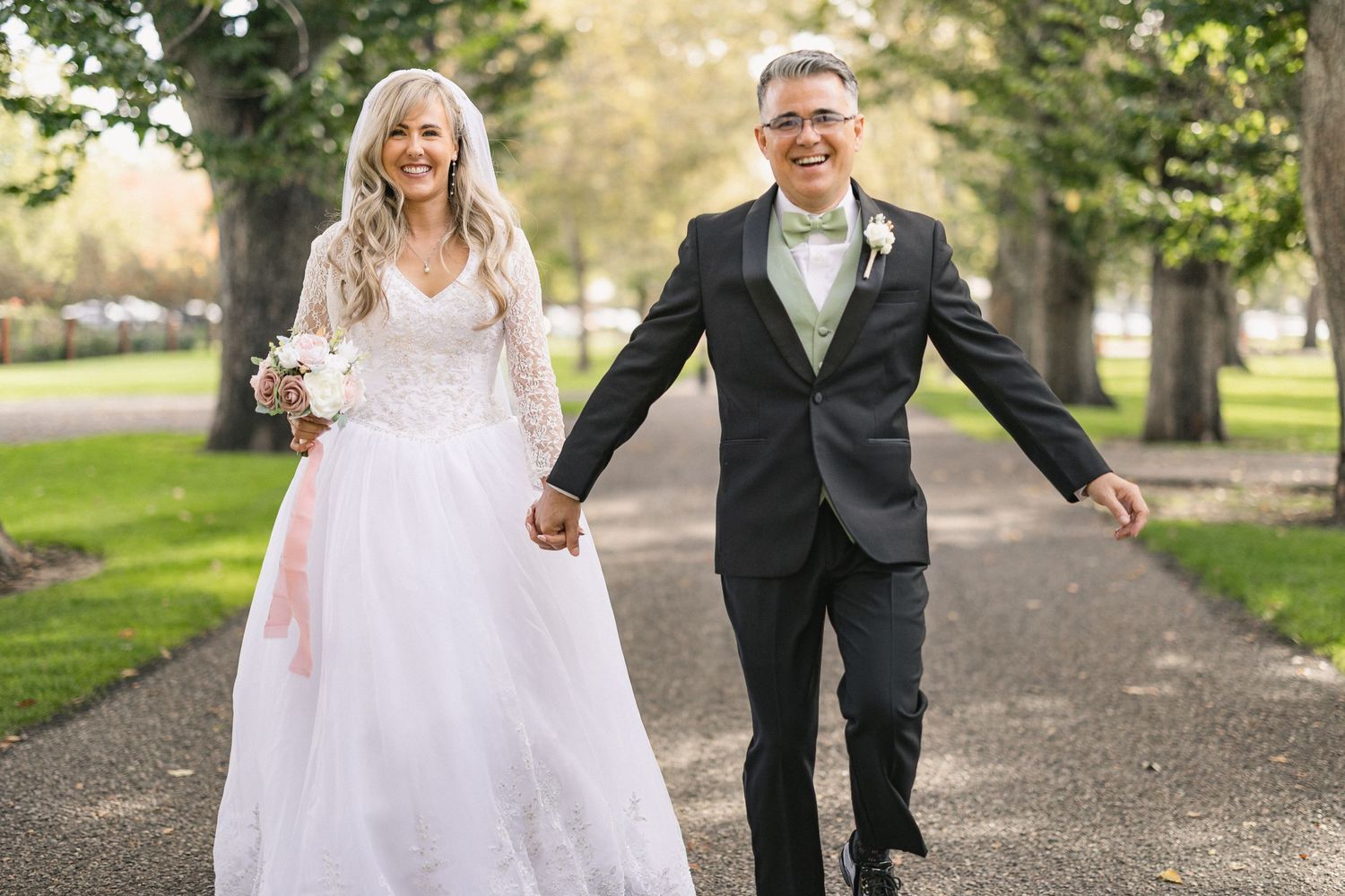 Joyful couple sharing a playful moment on their wedding day in a park setting.