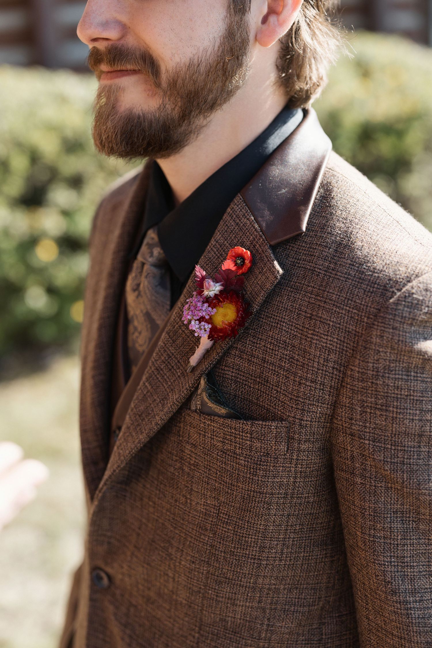 Close-up detail of brown tweed suit jacket with colorful floral boutonniere.