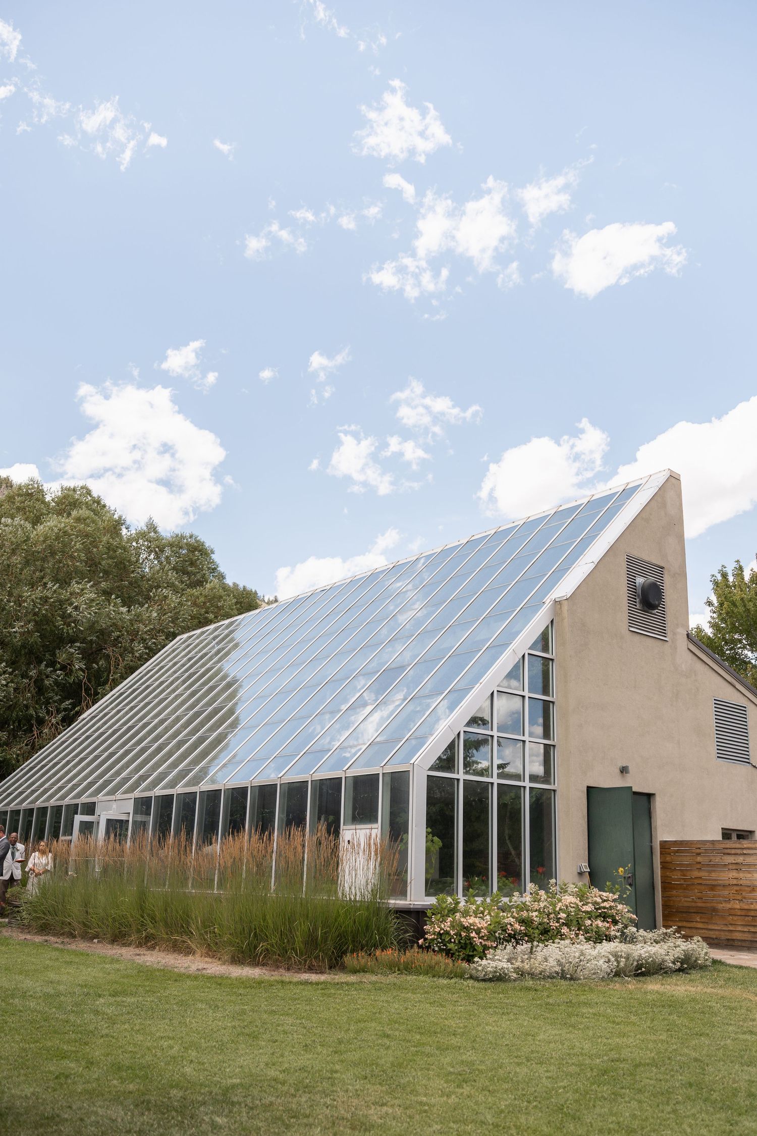 Modern greenhouse building with angled glass roof panels set against blue sky.