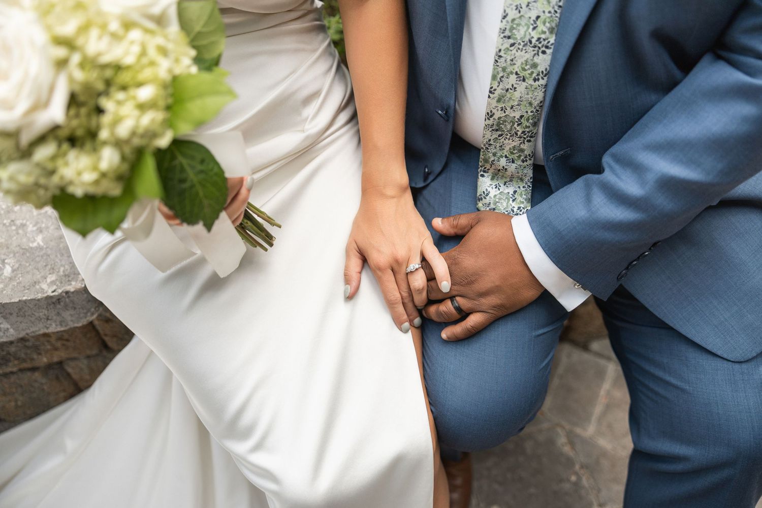 Wedding couple holds hands showing elegant attire with white dress and navy suit details.