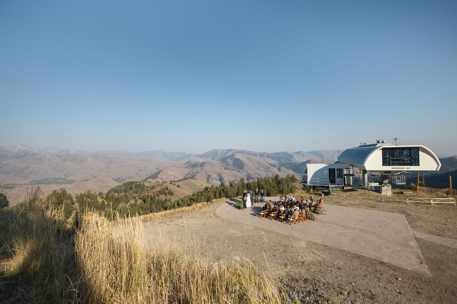 A scenic panoramic view of brown rolling hills and mountains stretches across a desert landscape under a blue sky.