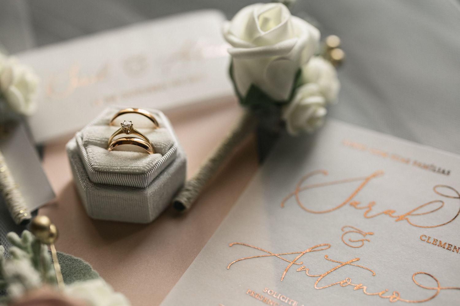Wedding invitation with gold lettering and ring box decorated with white roses.