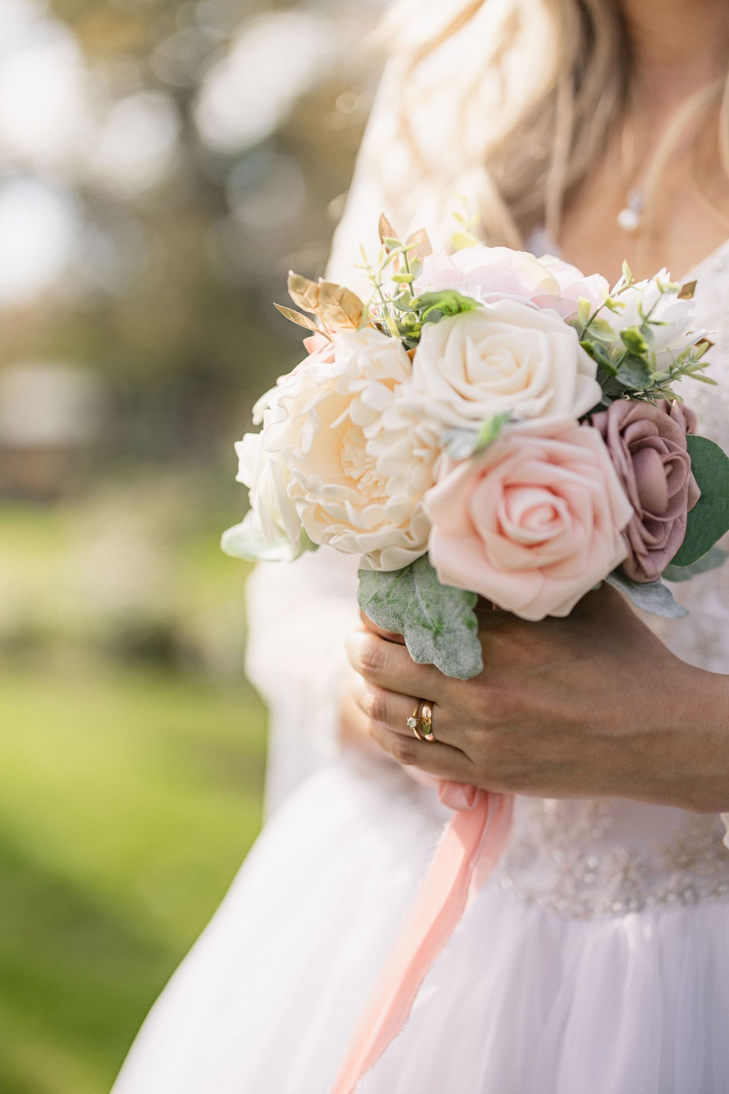 Elegant bridal bouquet featuring cream and blush roses with eucalyptus leaves against a soft bokeh background.