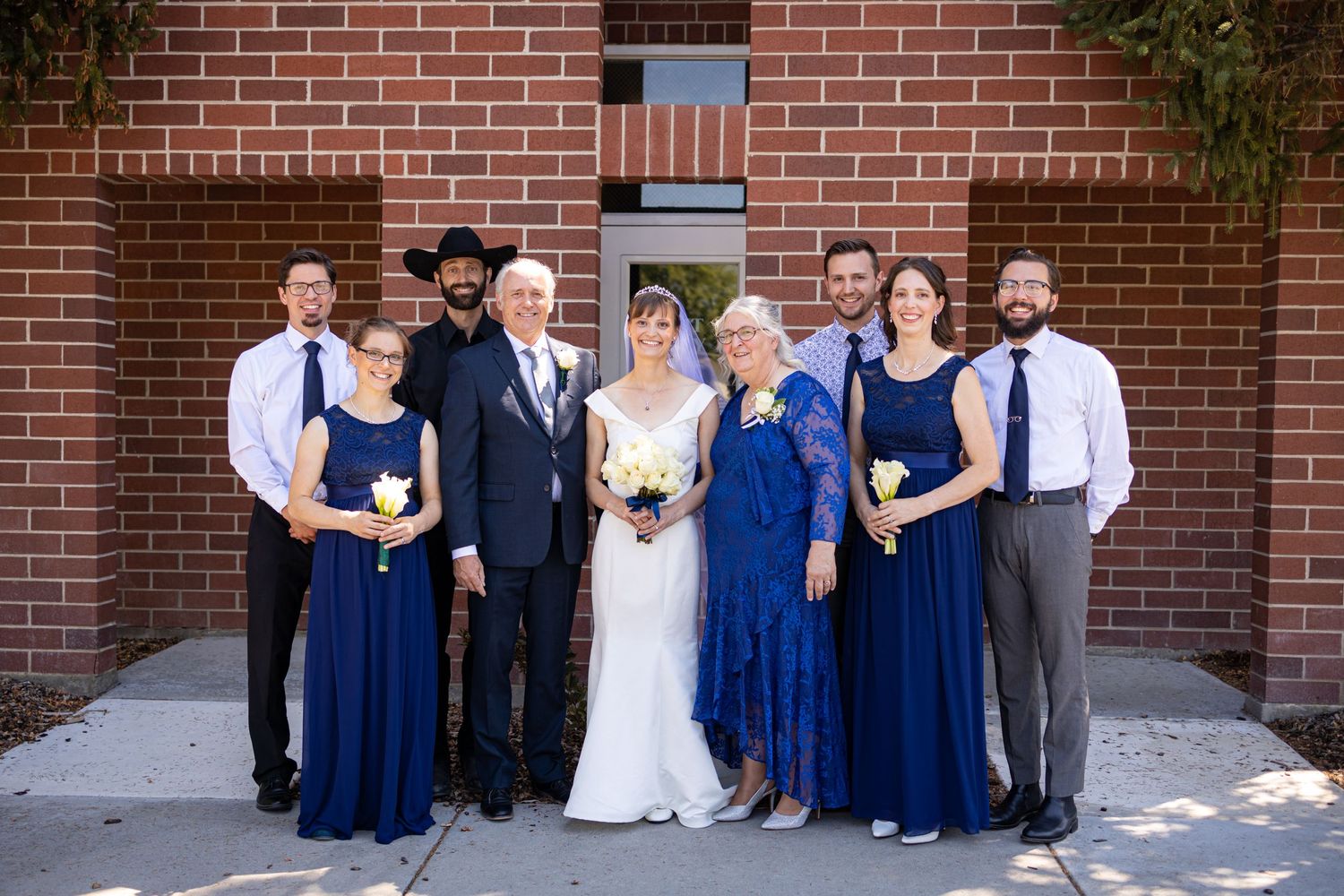 Wedding party in navy and black formal attire poses together against brick building.