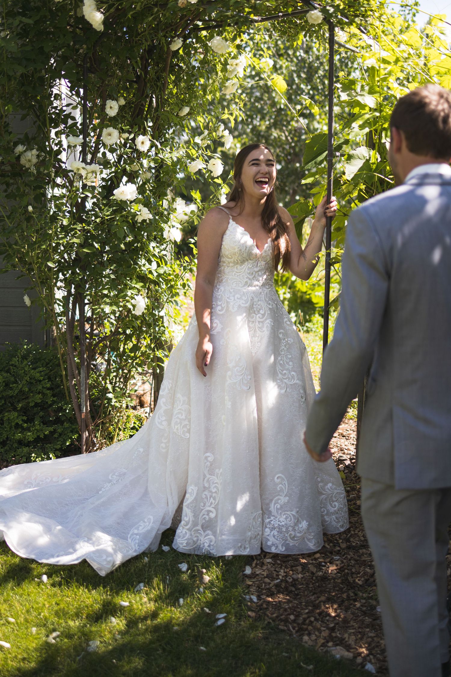 A wedding first look moment captured under a floral arch in a sunlit garden.