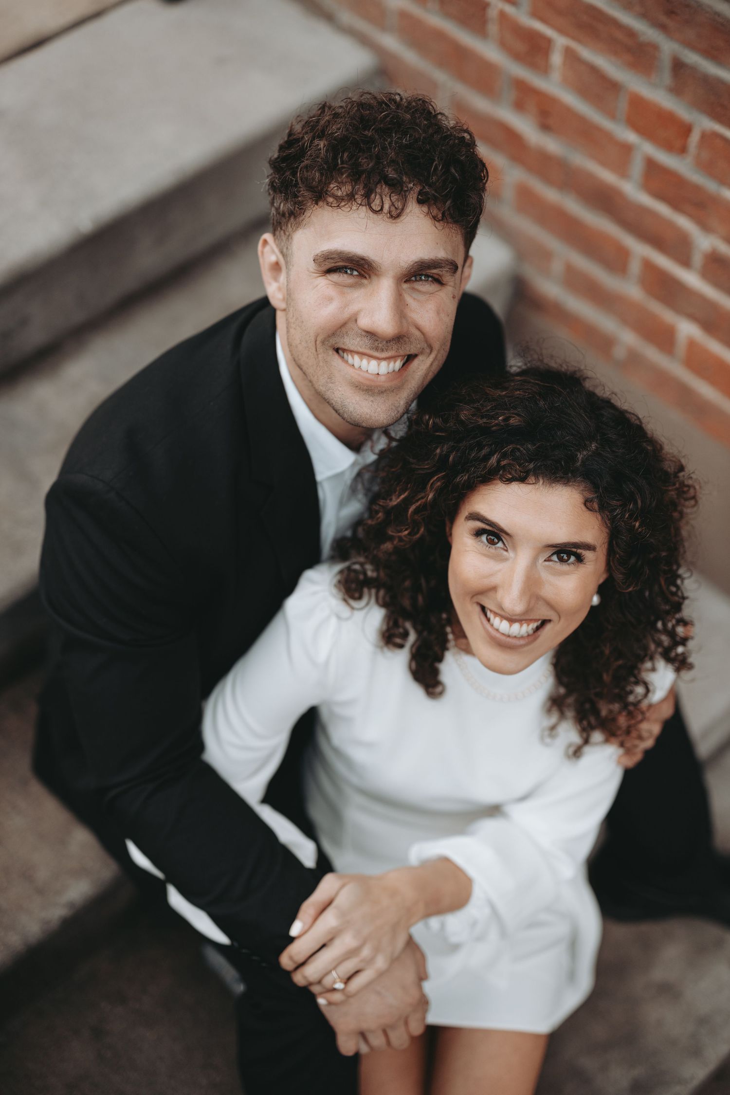 A happy couple in formal wear sharing an intimate moment on urban steps.