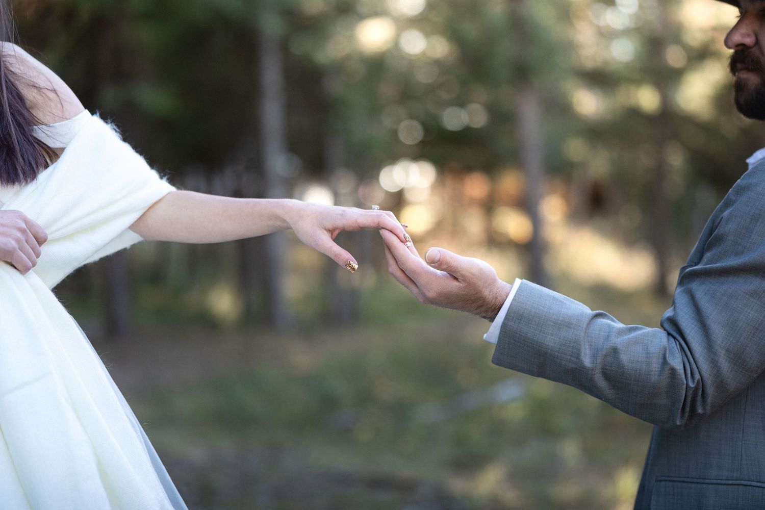 Artistic shot of bride and groom's hands meeting during outdoor wedding ceremony.