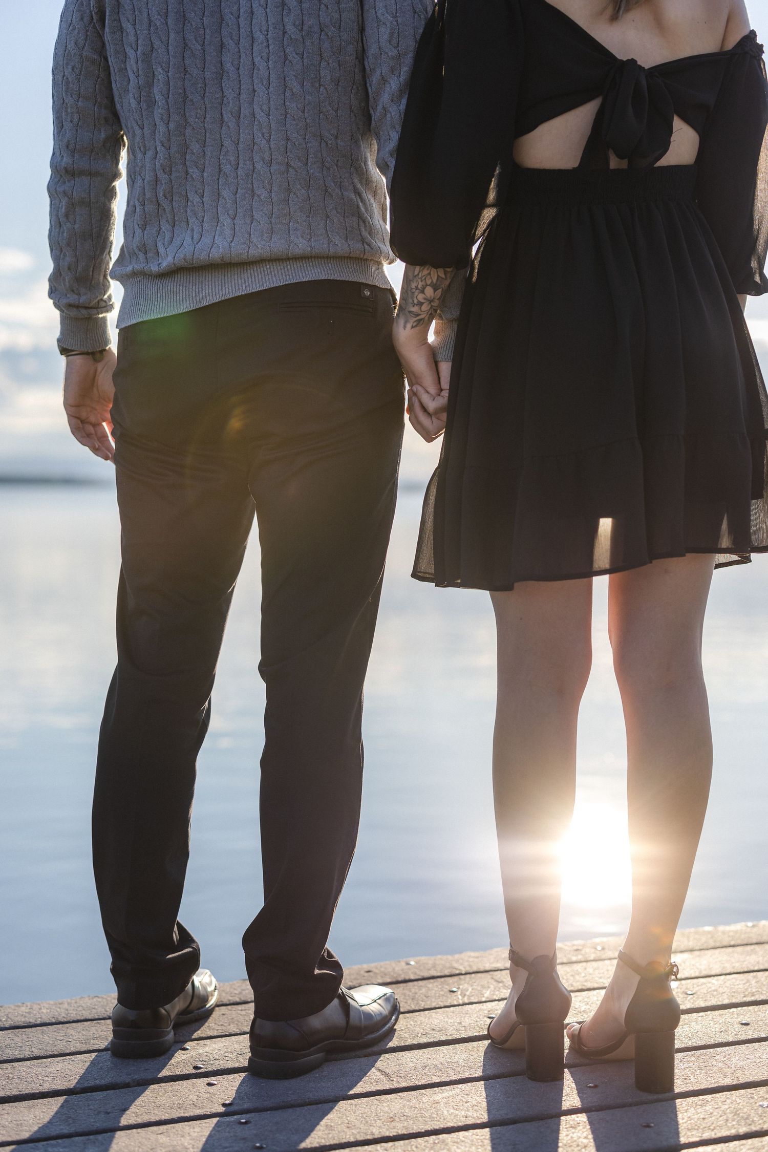 Silhouetted couple standing hand in hand on a lakeside dock during golden hour.