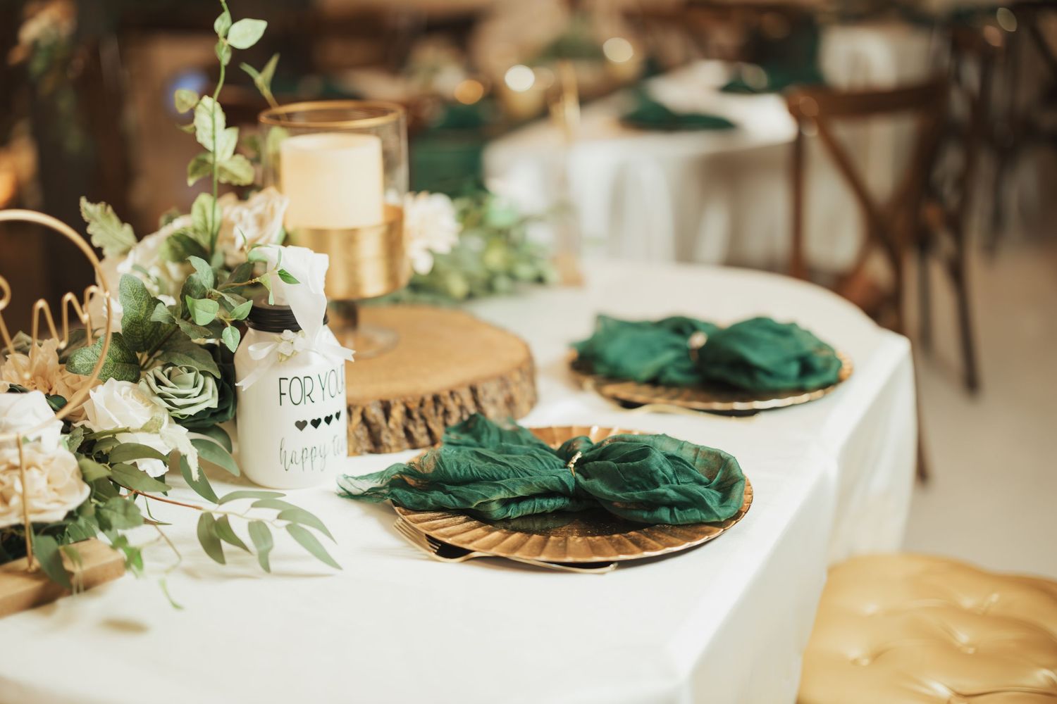 Elegant wedding table setting with emerald napkins and greenery centerpiece.