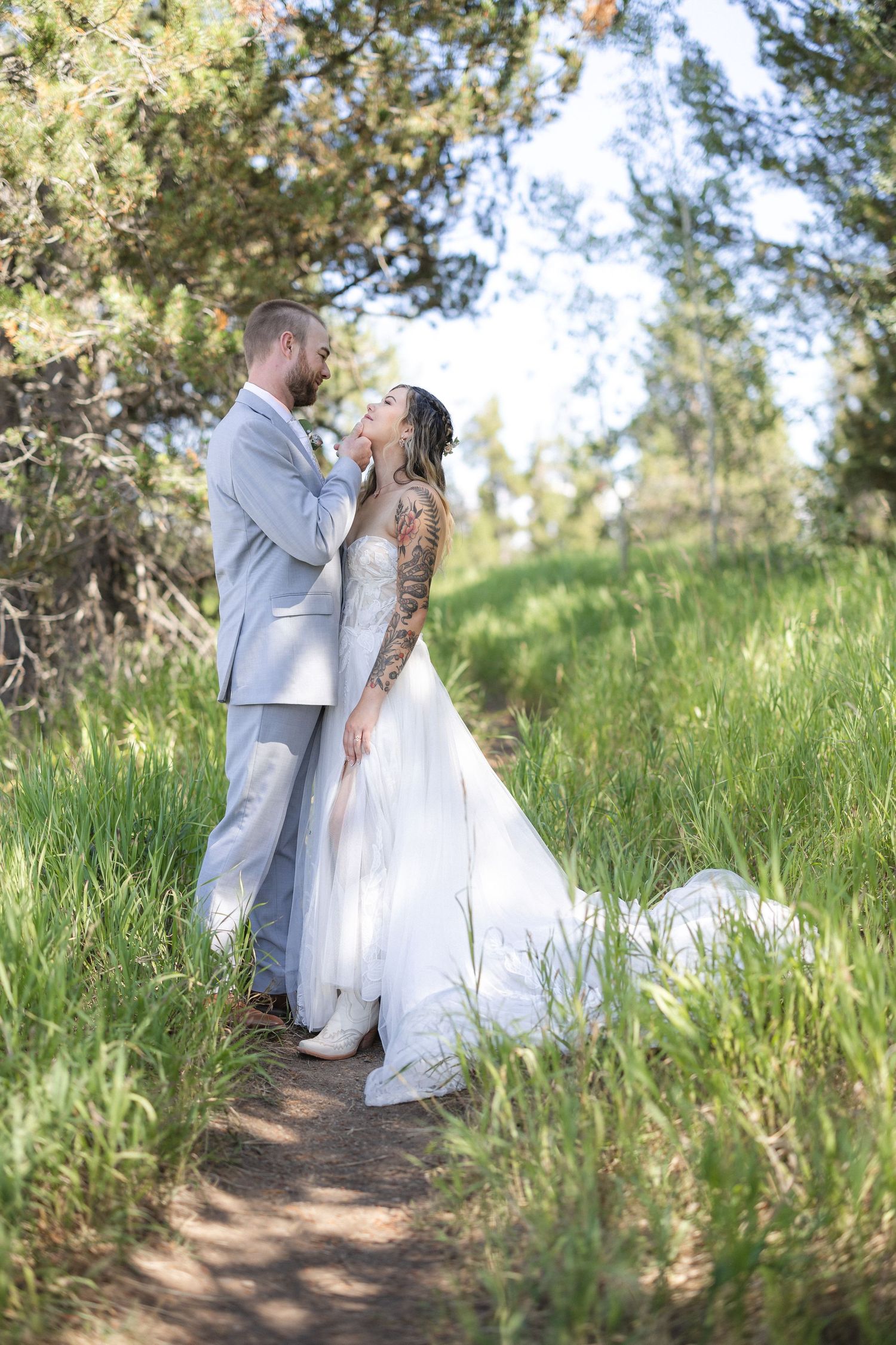 Wedding couple poses playfully on a forest path surrounded by tall grass.