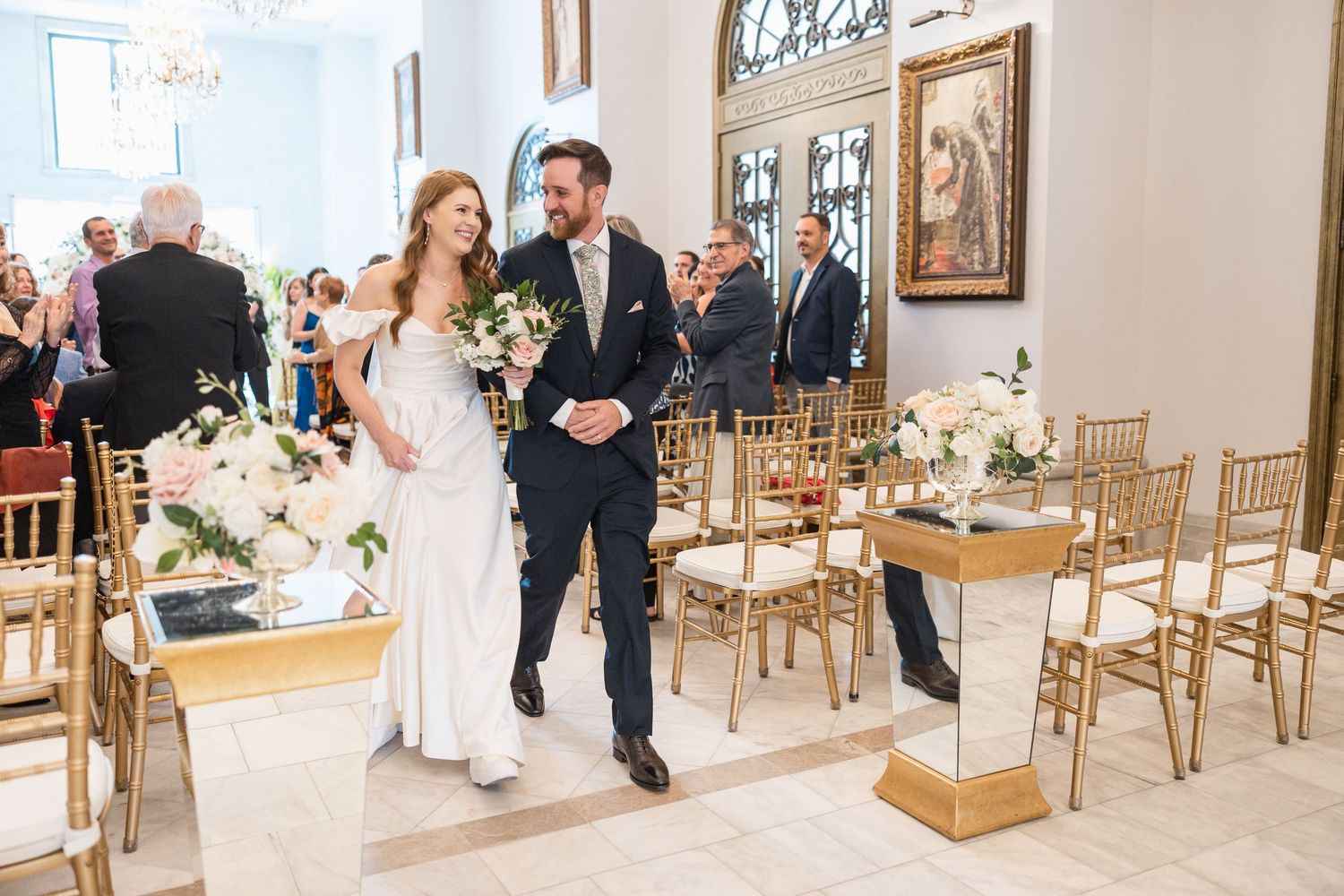 Long aisle view of a wedding ceremony venue with gold chairs and floral arrangements.