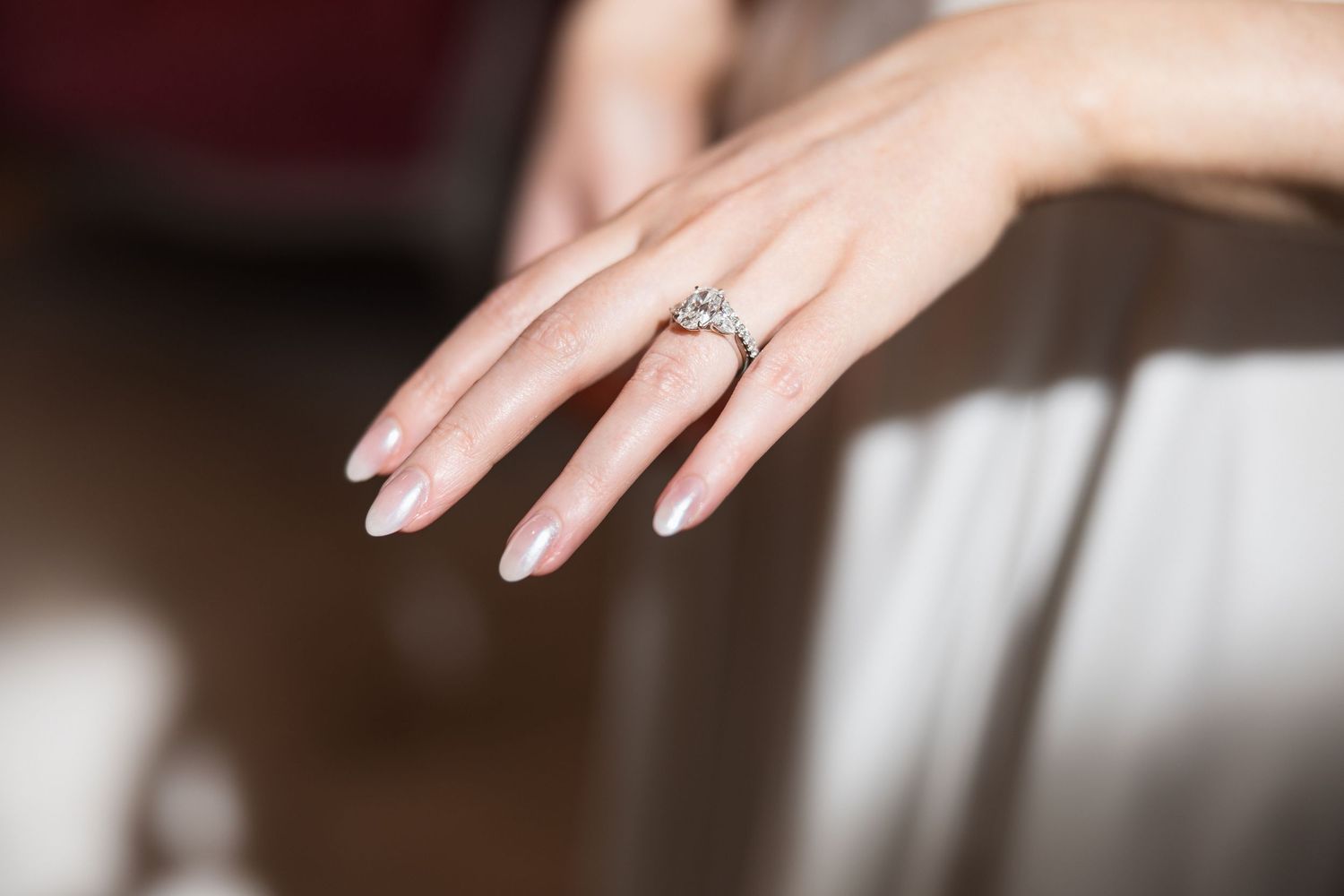 Close-up of engagement ring and manicured hands in natural light.