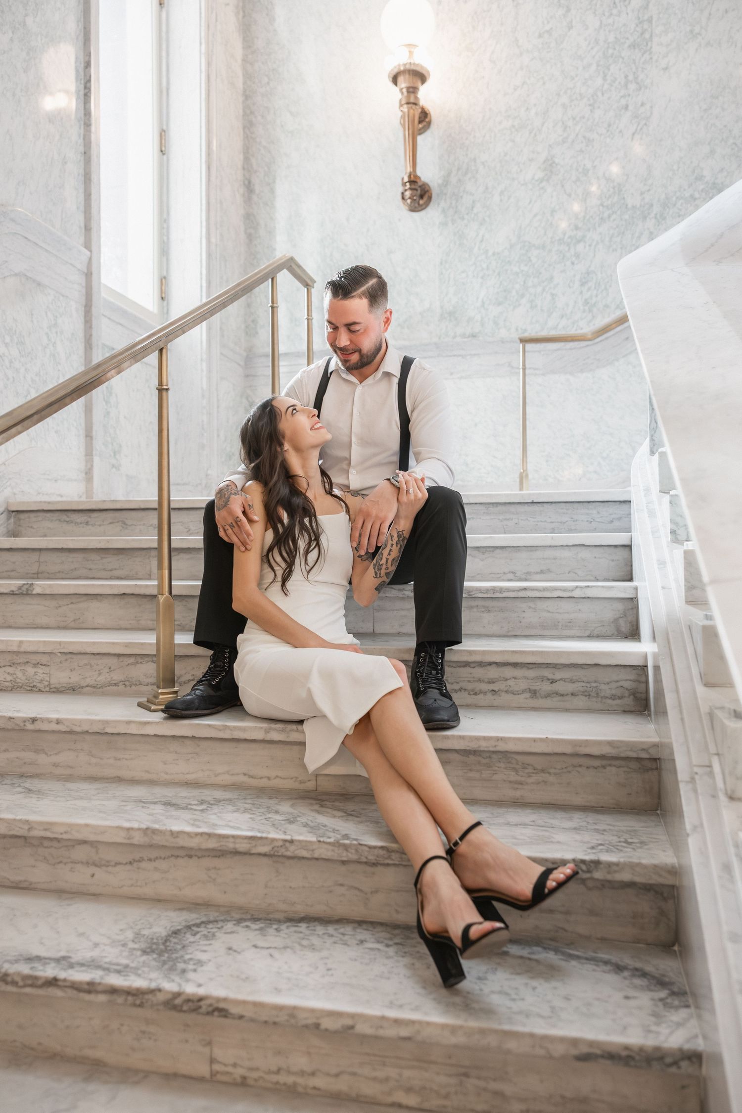 Couple sits casually on marble stairs in formal attire during wedding photoshoot.