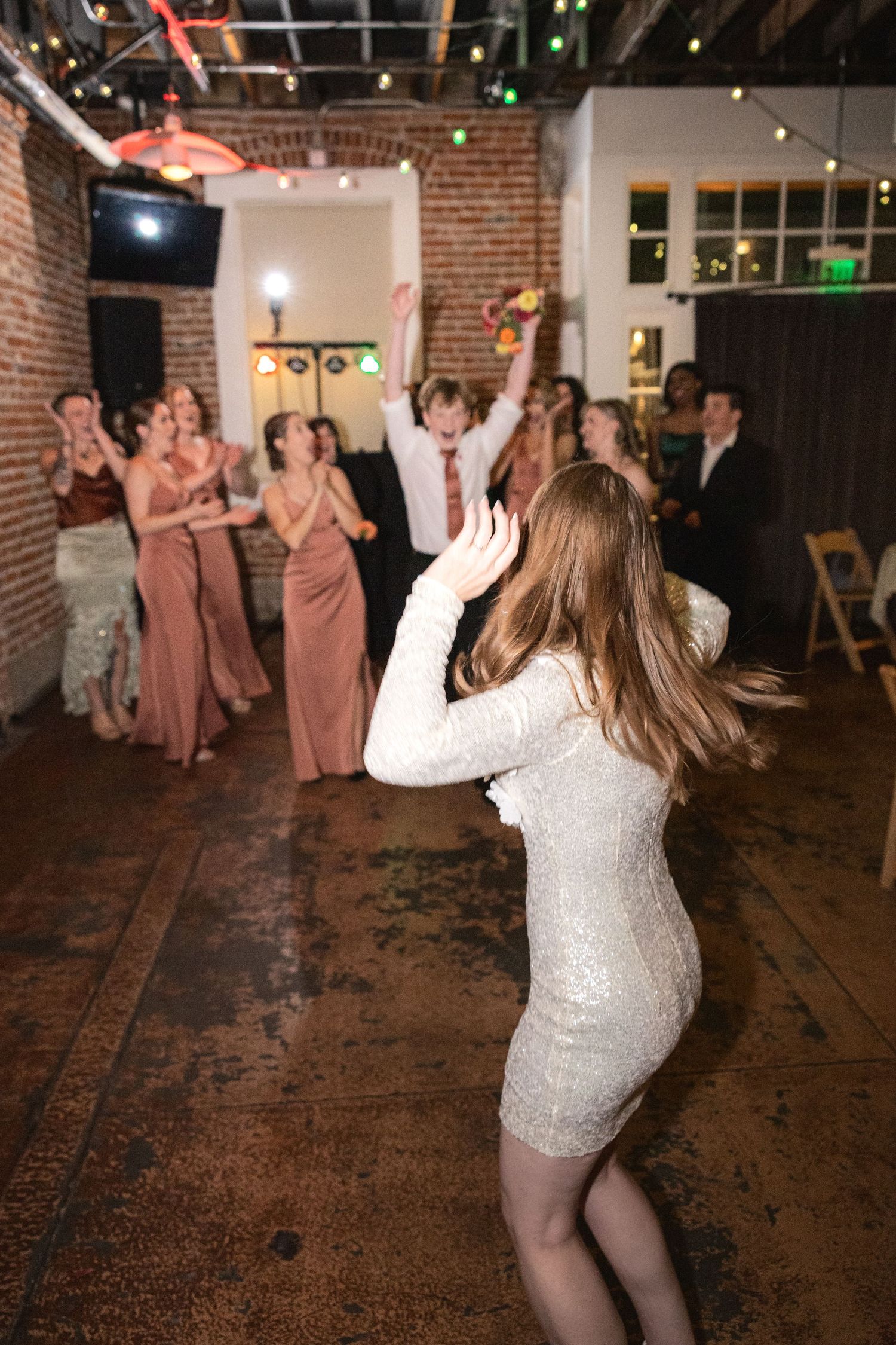 Energetic dance party with guests in mauve dresses on a rustic brick floor.