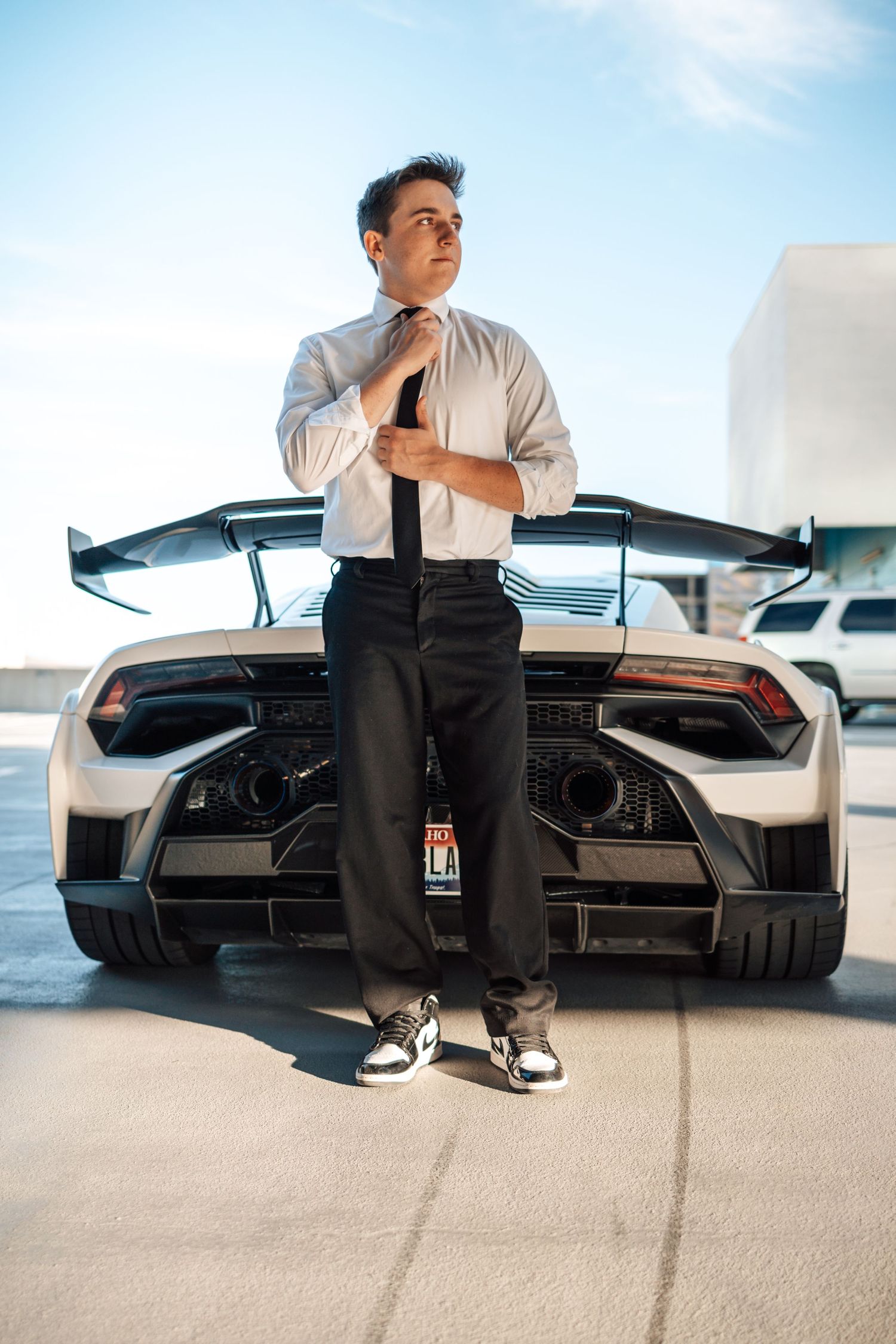 Person in white shirt and tie standing in front of luxury car with raised wing.