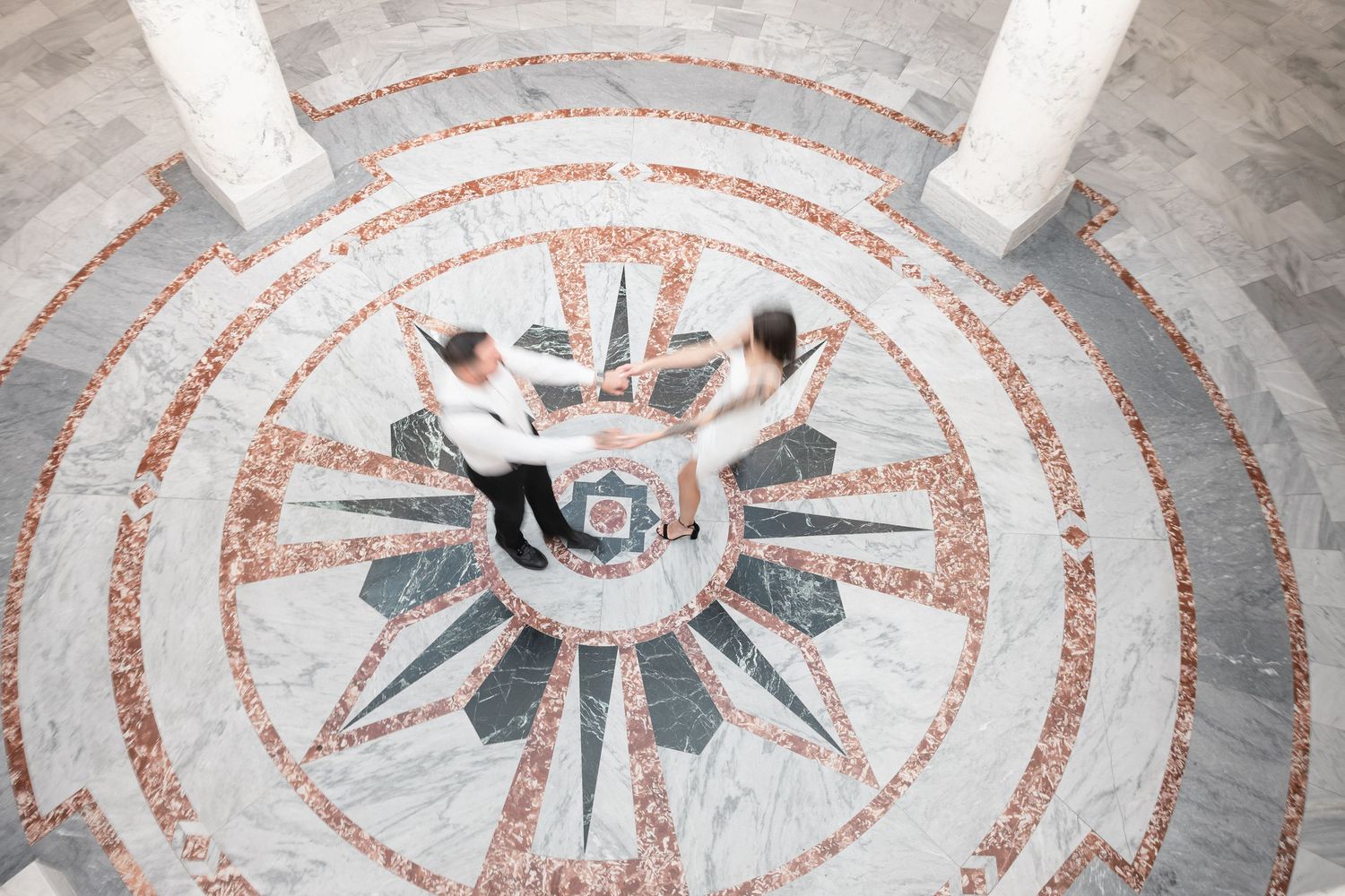 Decorative circular mosaic floor pattern with black and terracotta geometric designs on white marble background.
