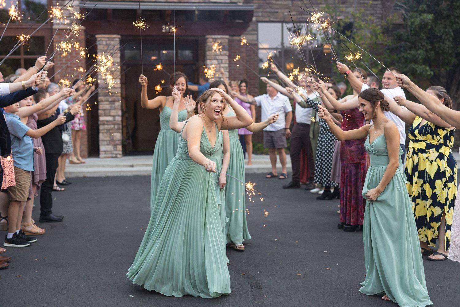 Bridesmaids in mint green dresses dance through sparkler tunnel during wedding exit.