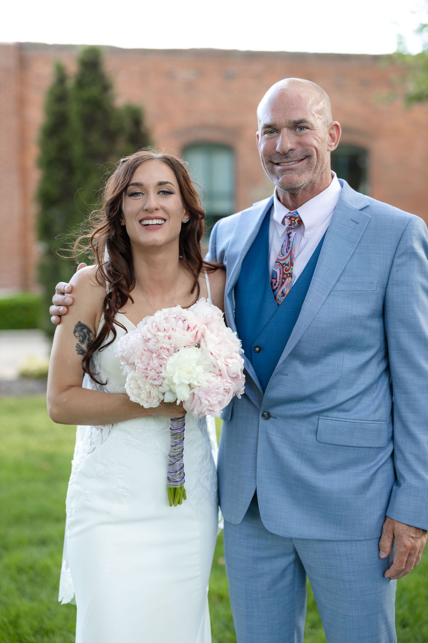 Wedding portrait with elegant white dress and light blue suit against brick wall background.