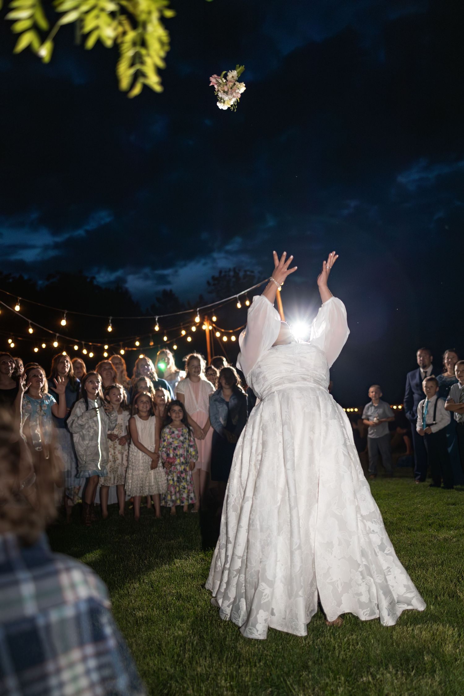 White-clad figures dancing in a grassy field under bistro lights at night.