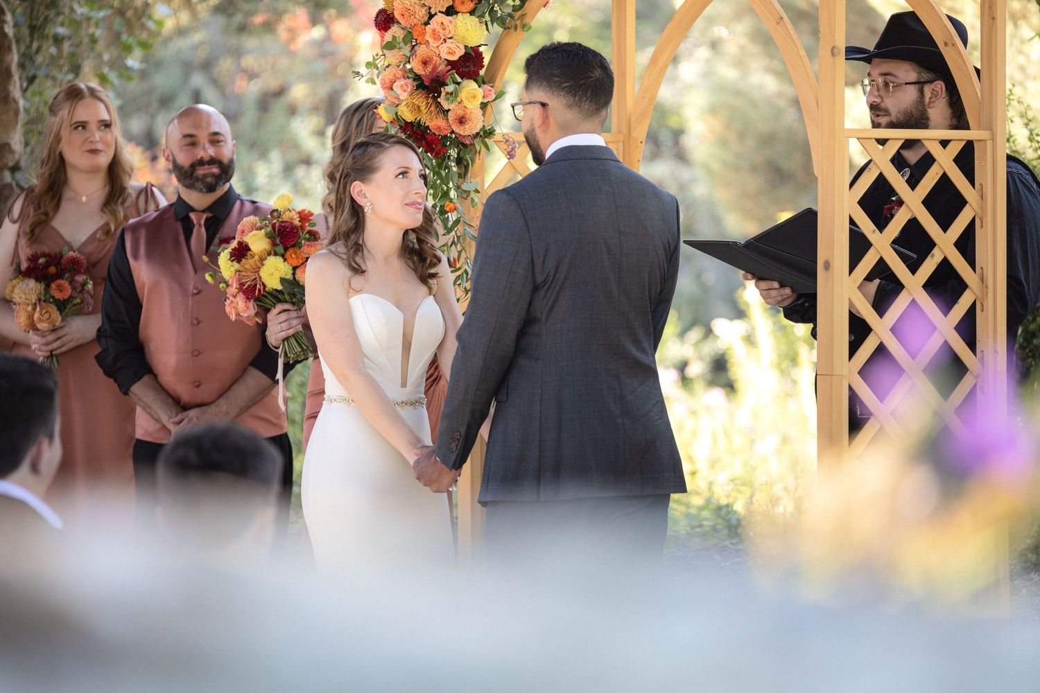 Wedding ceremony under floral arch with autumn-colored decorations.