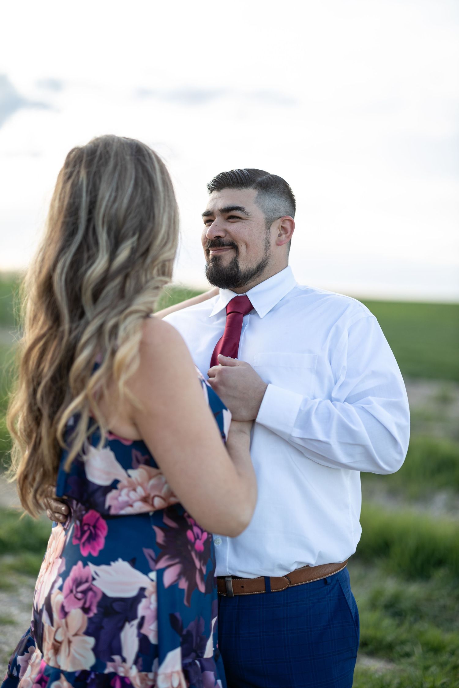 Couple in floral dress and business attire dancing outdoors on natural path.