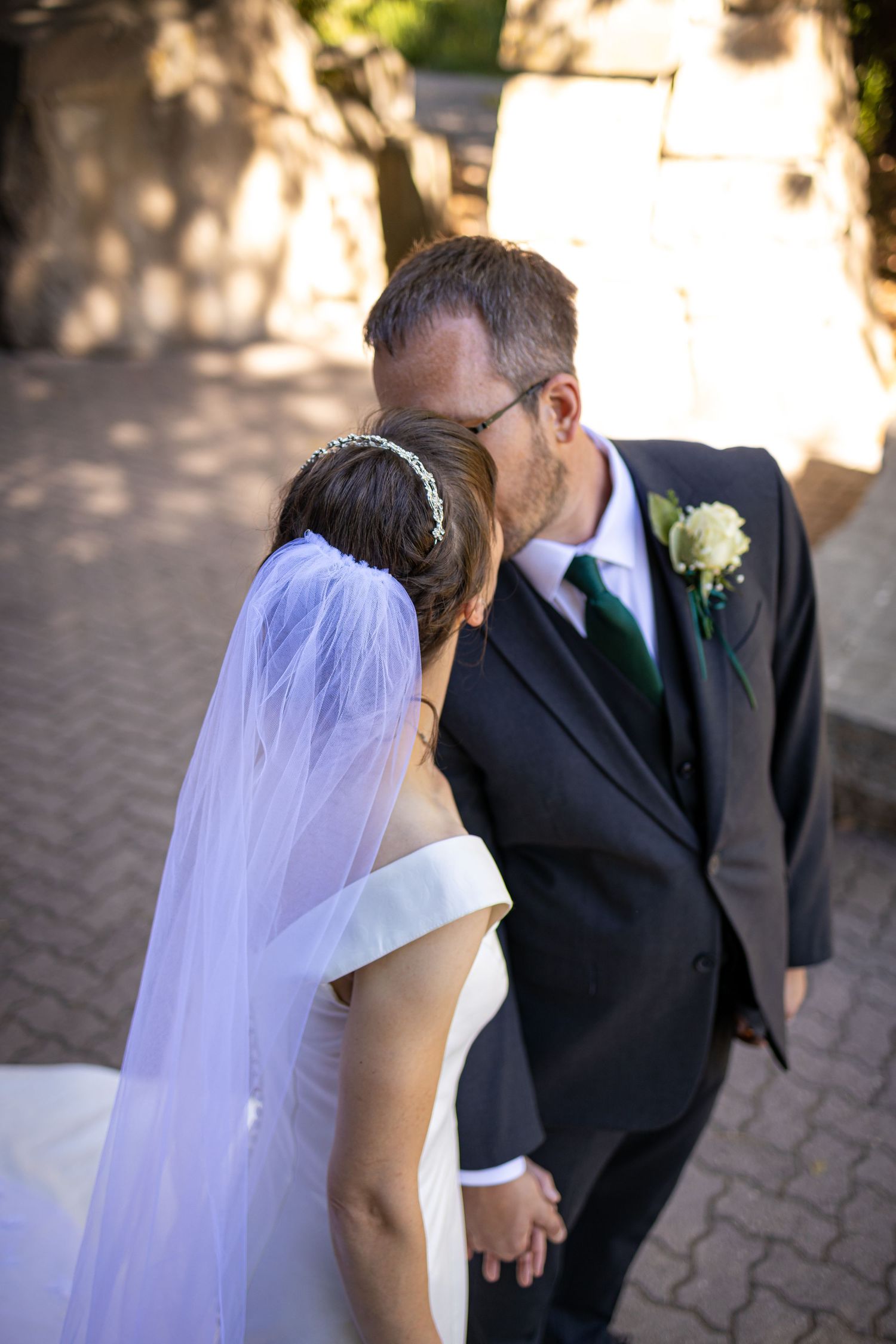 Newlywed couple shares an intimate moment on a brick pathway with the groom wearing a boutonniere.