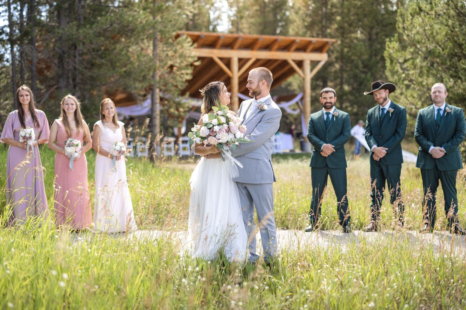 Candid outdoor wedding party photo with bridesmaids and groomsmen posing in a natural setting.