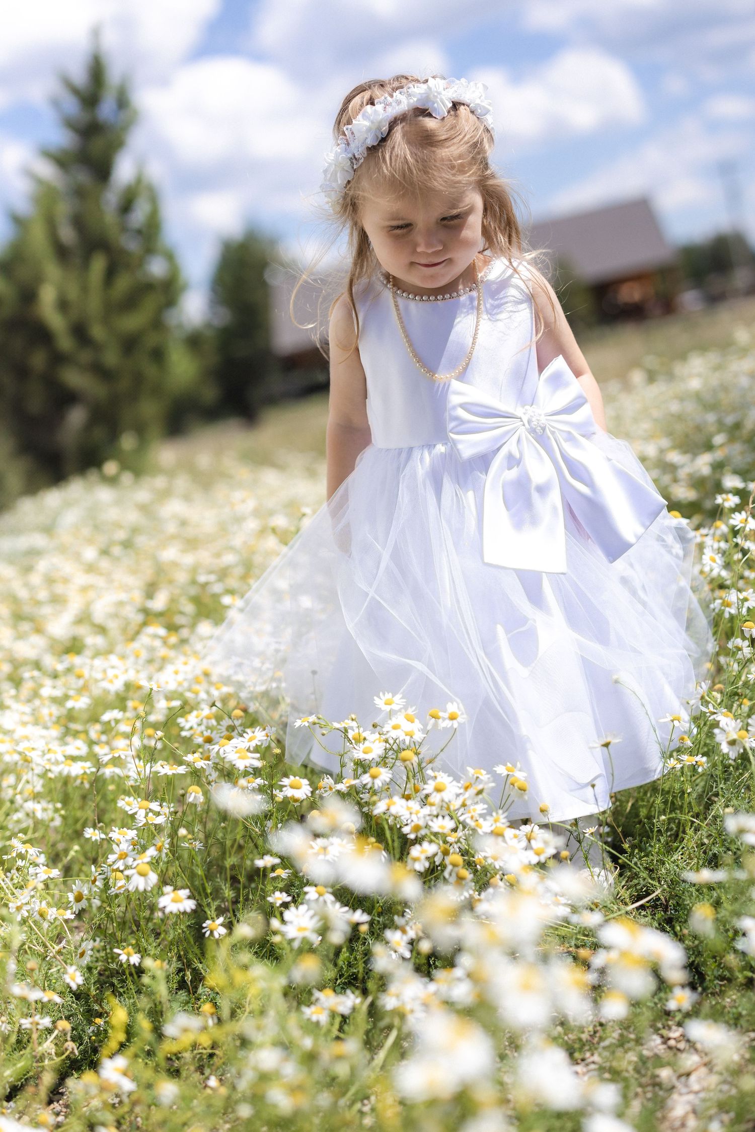 A young flower girl in a white dress explores a field of daisies during a wedding celebration.