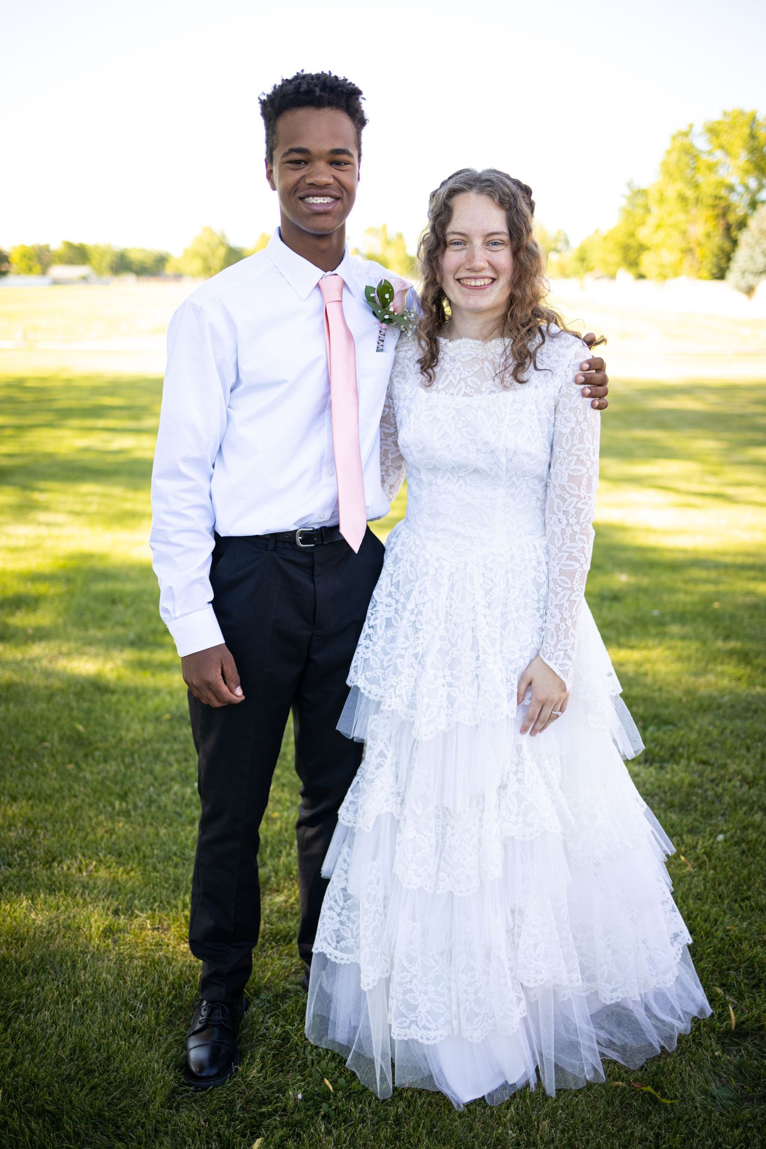 Wedding couple poses together on grassy lawn during outdoor summer ceremony.