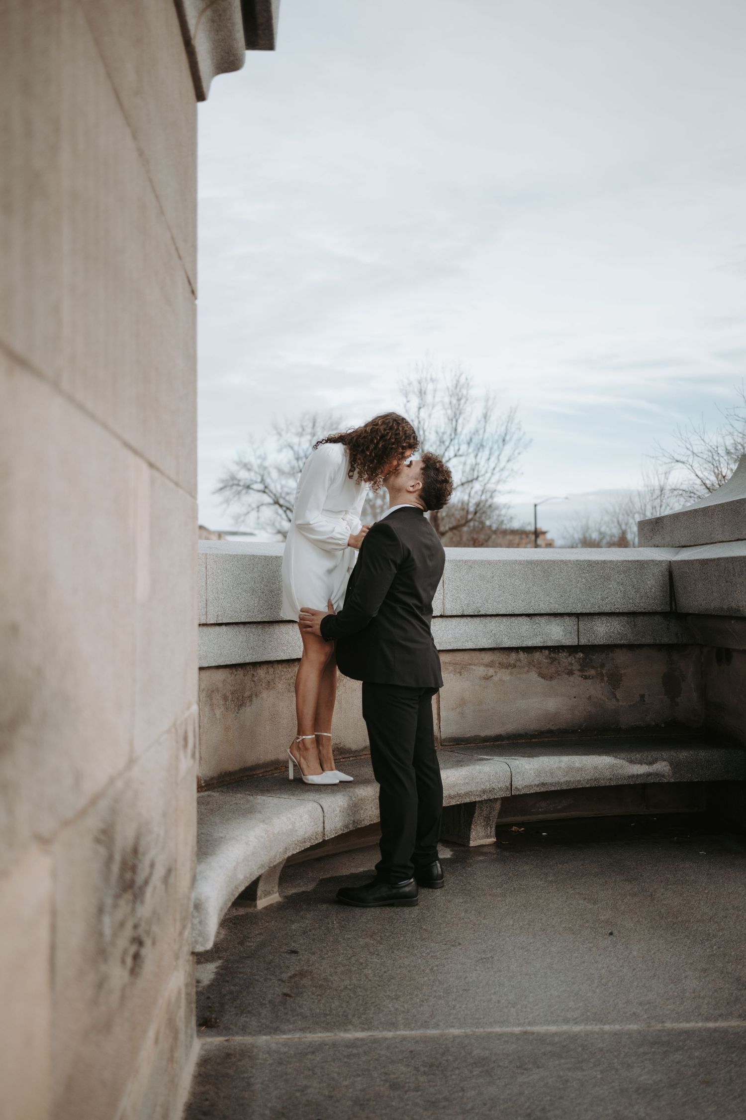 A couple shares a romantic moment on a curved stone balcony.