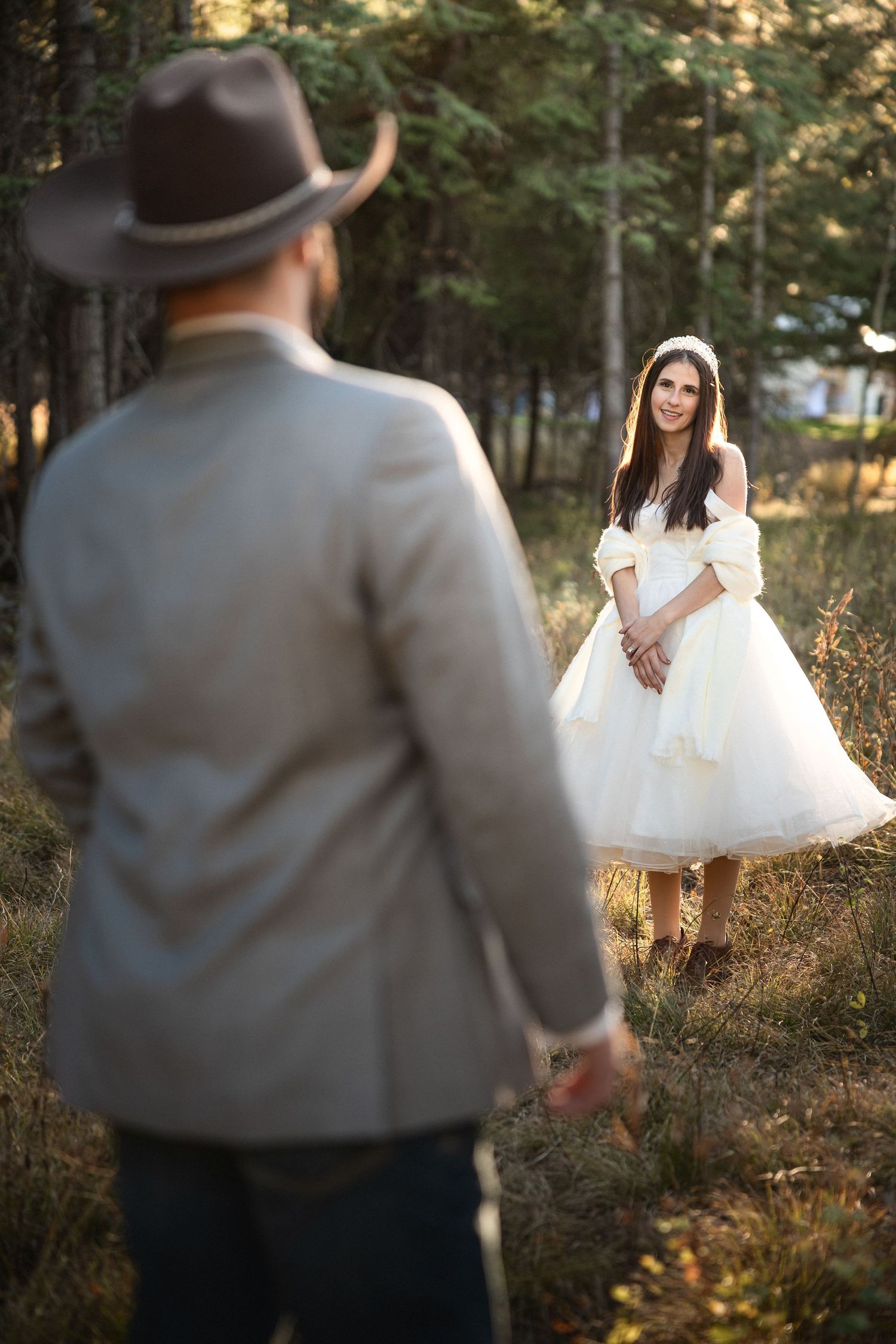 Rustic wedding scene with bride in tea-length dress and groom in cowboy hat.