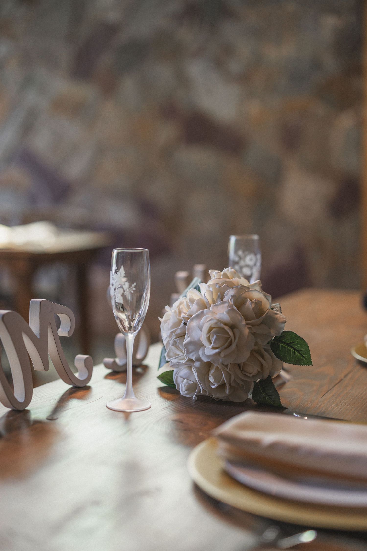 White rose bouquet with champagne glasses and place settings on rustic wooden table.